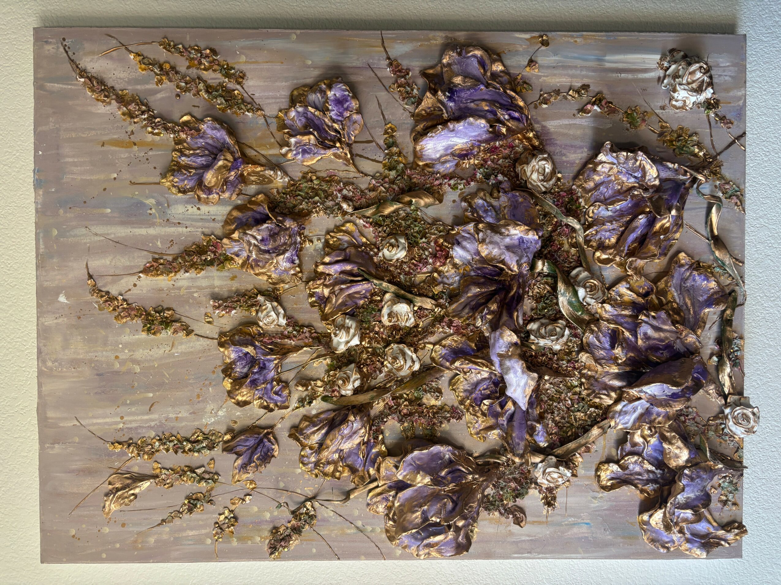 Arrangement of purple and silver flowers with gold accents on a light background.
