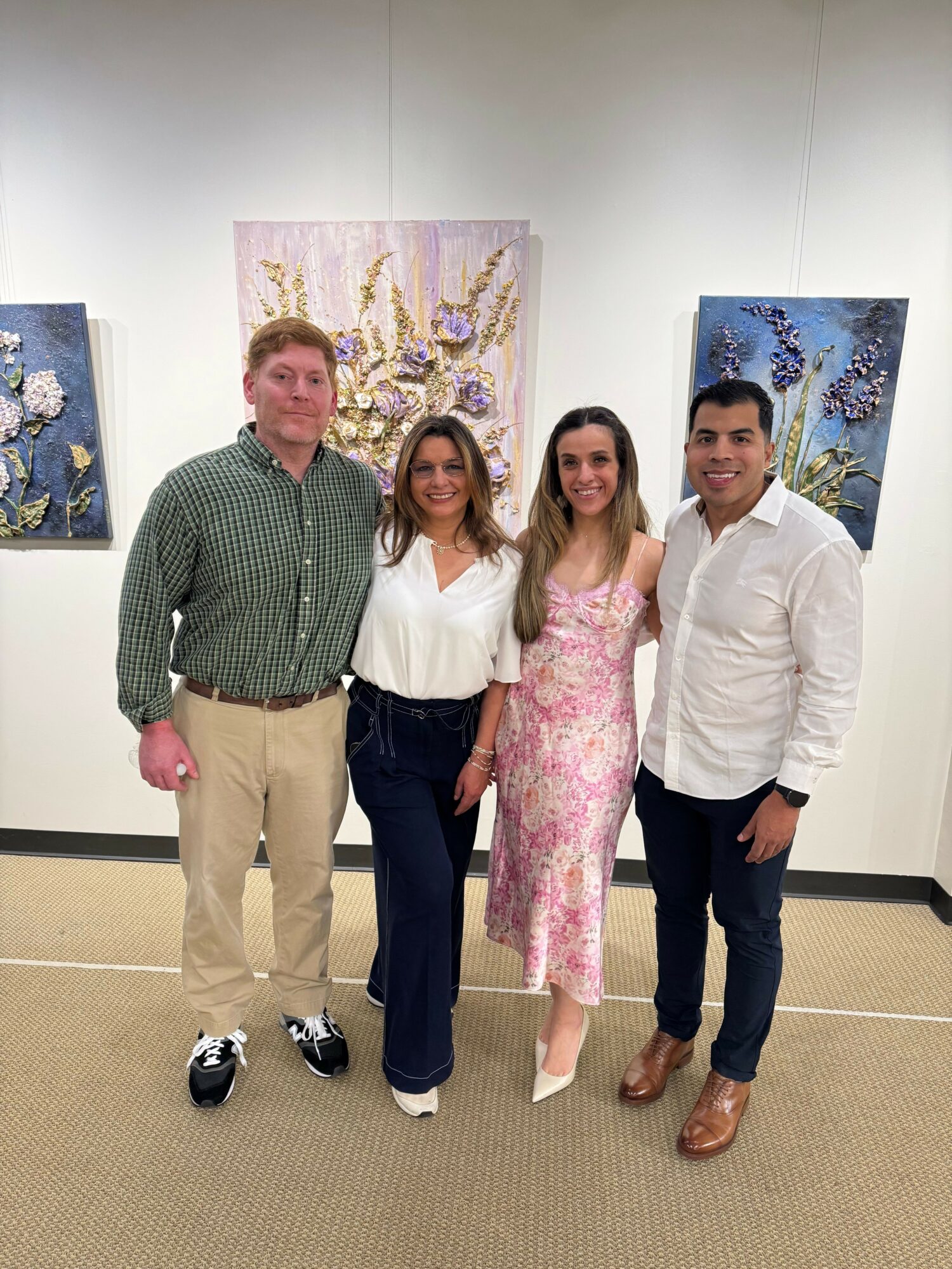 Four people standing in an art gallery with floral paintings behind them, smiling at the camera.