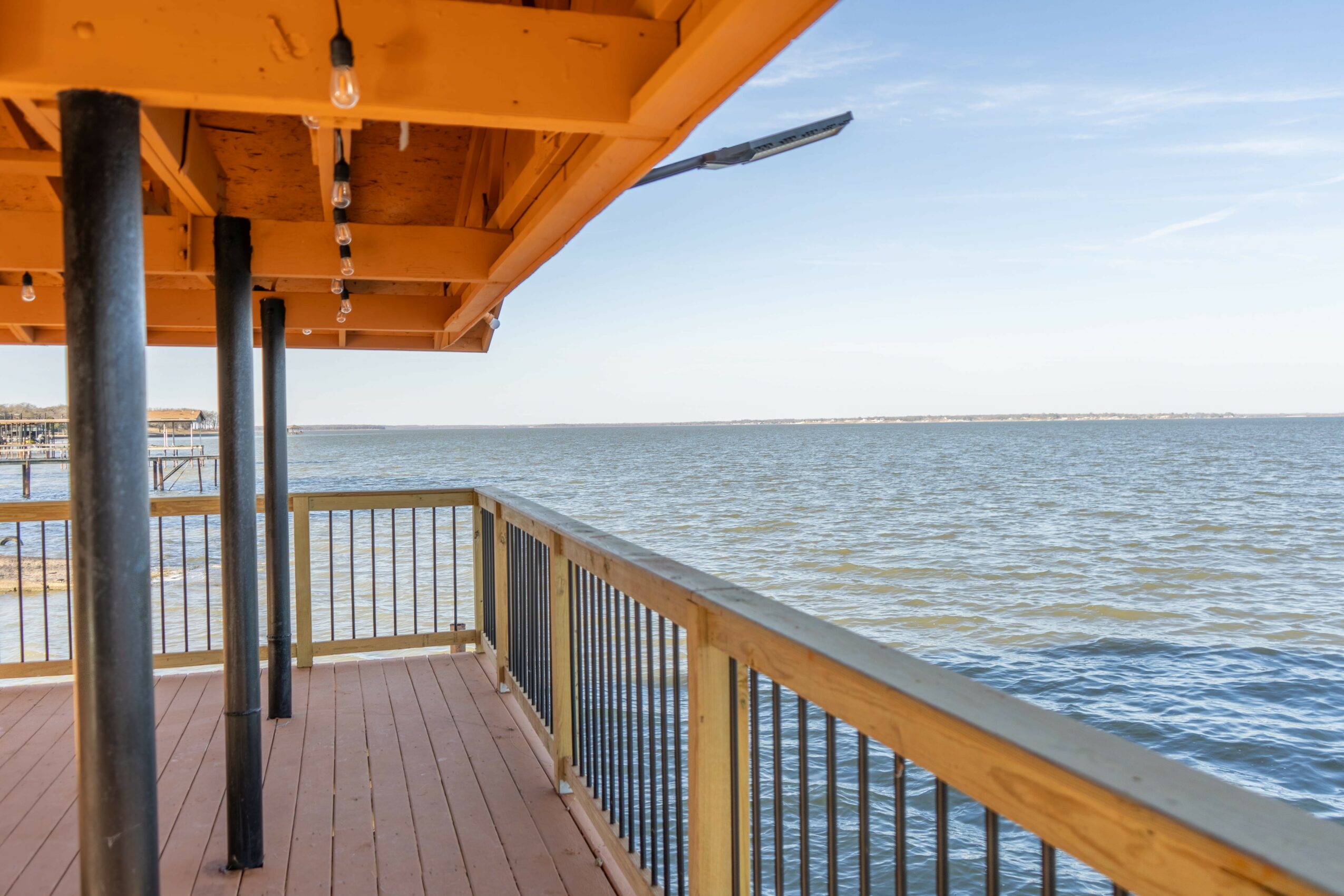 View from a wooden deck overlooking a body of water with a railing and a yellow roof overhang.