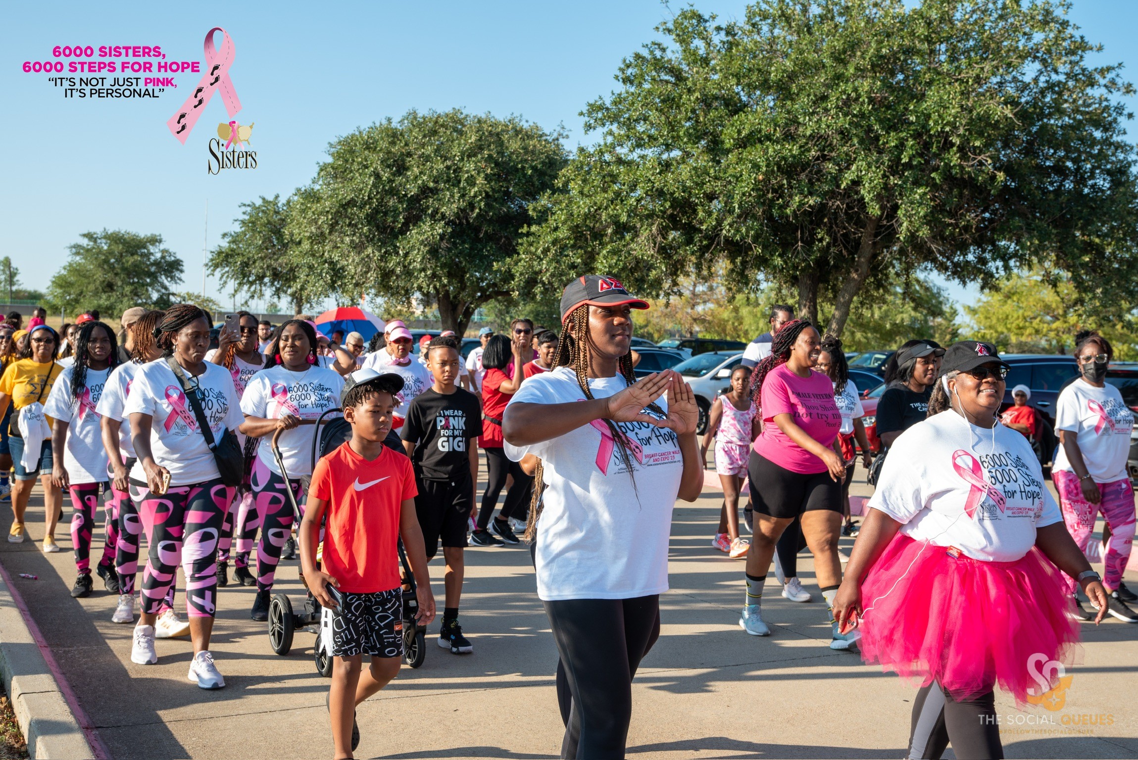 Group of people participating in a walk event outdoors, some wearing pink and white clothing, trees in background.
