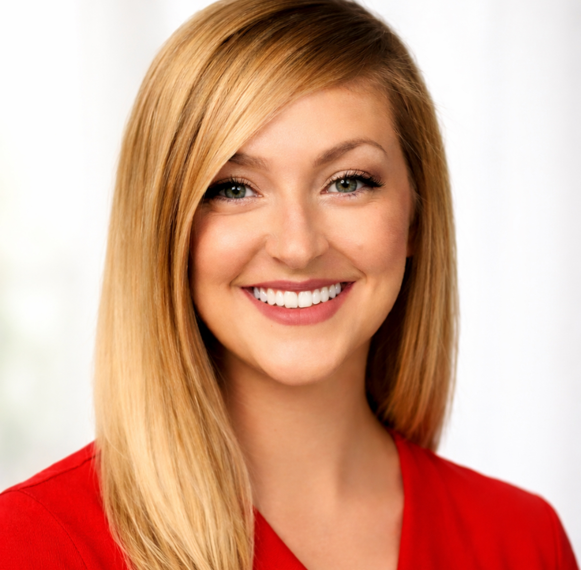 Young woman with long blonde hair smiling, wearing a red top, against a light background.
