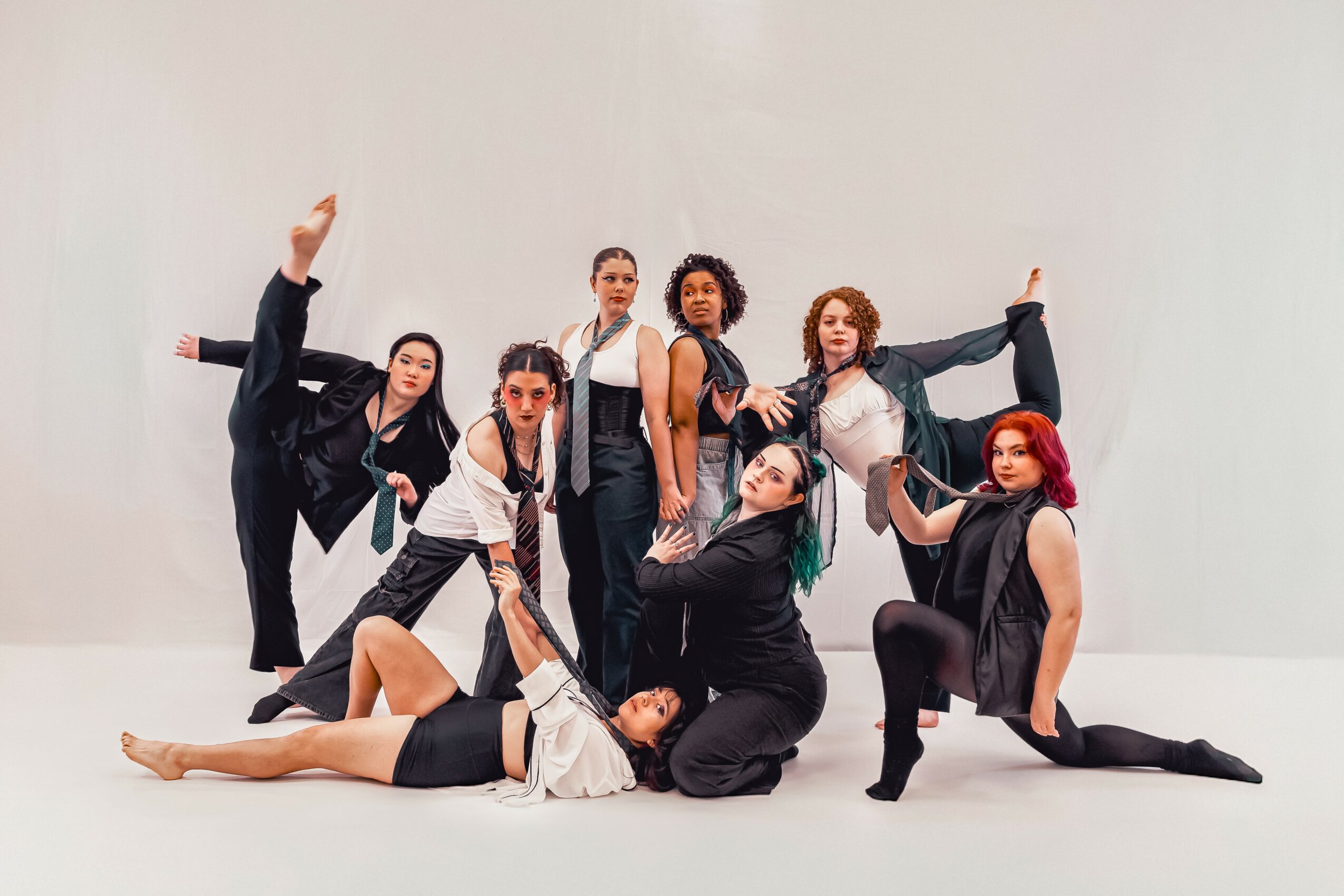 Group of nine women posing in dance or performance stance against a plain white background.