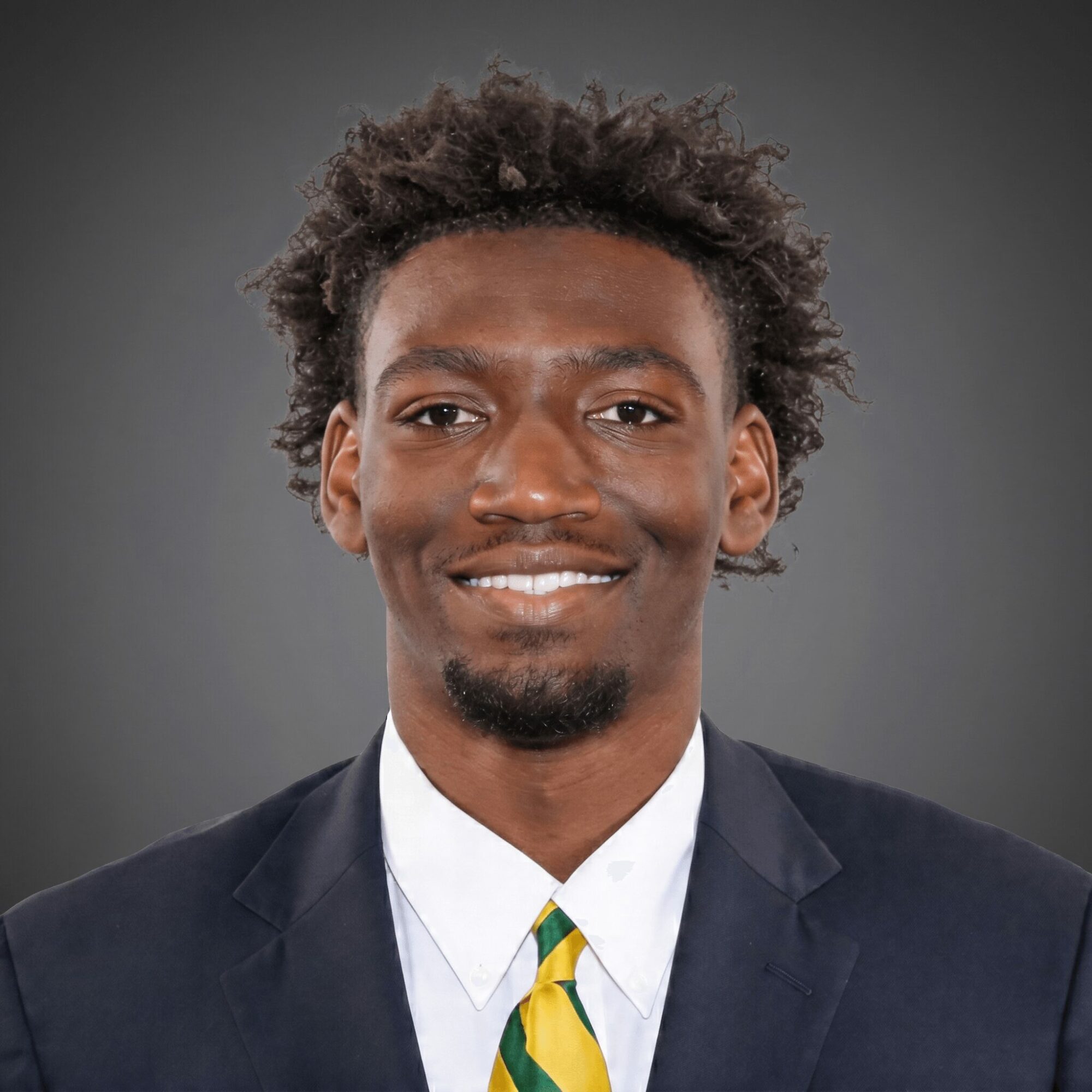Man in suit smiling, wearing a white shirt and yellow tie, against a gray background.