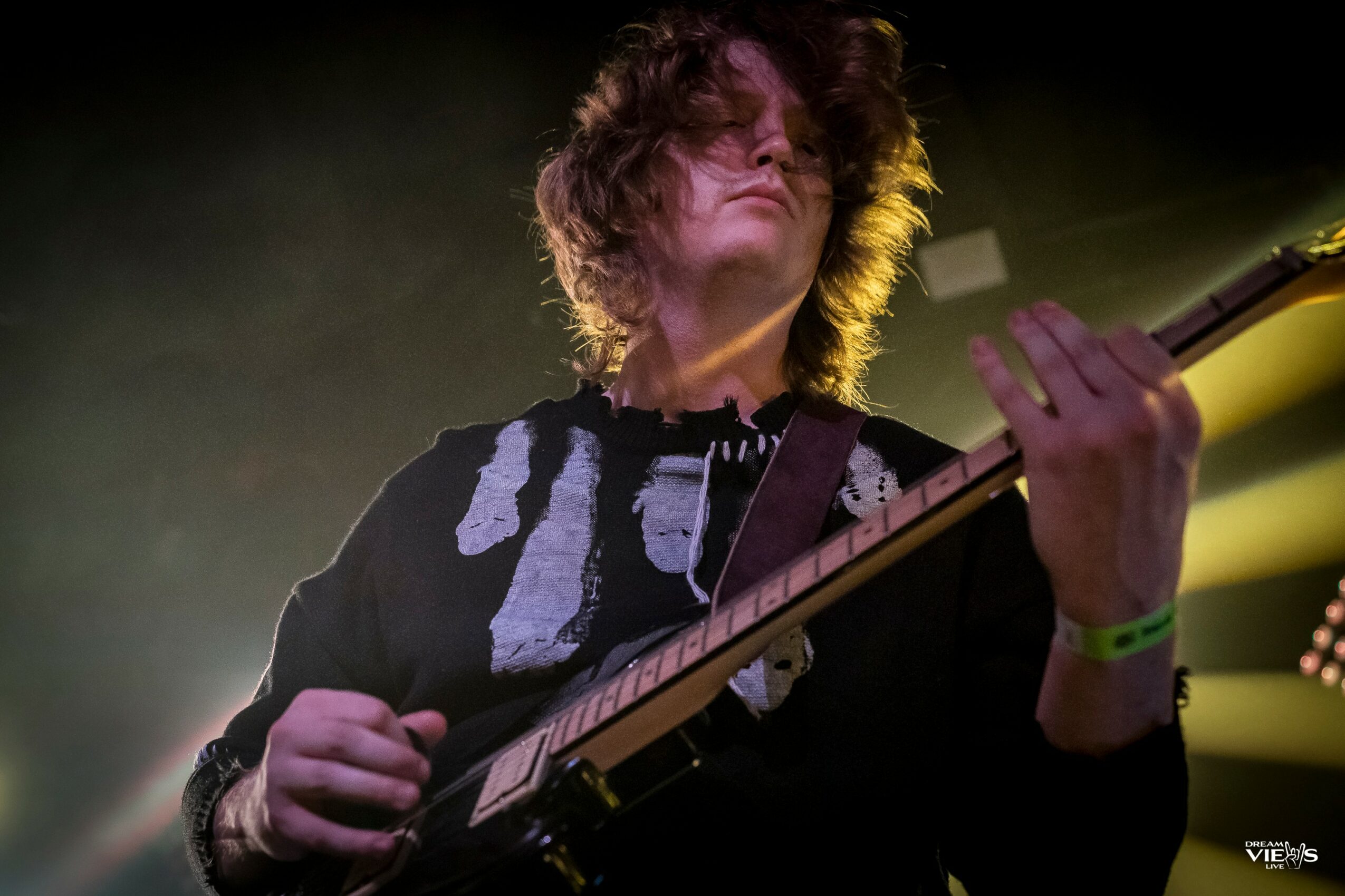 Person with curly hair playing an electric guitar on stage with yellow and green lighting effects