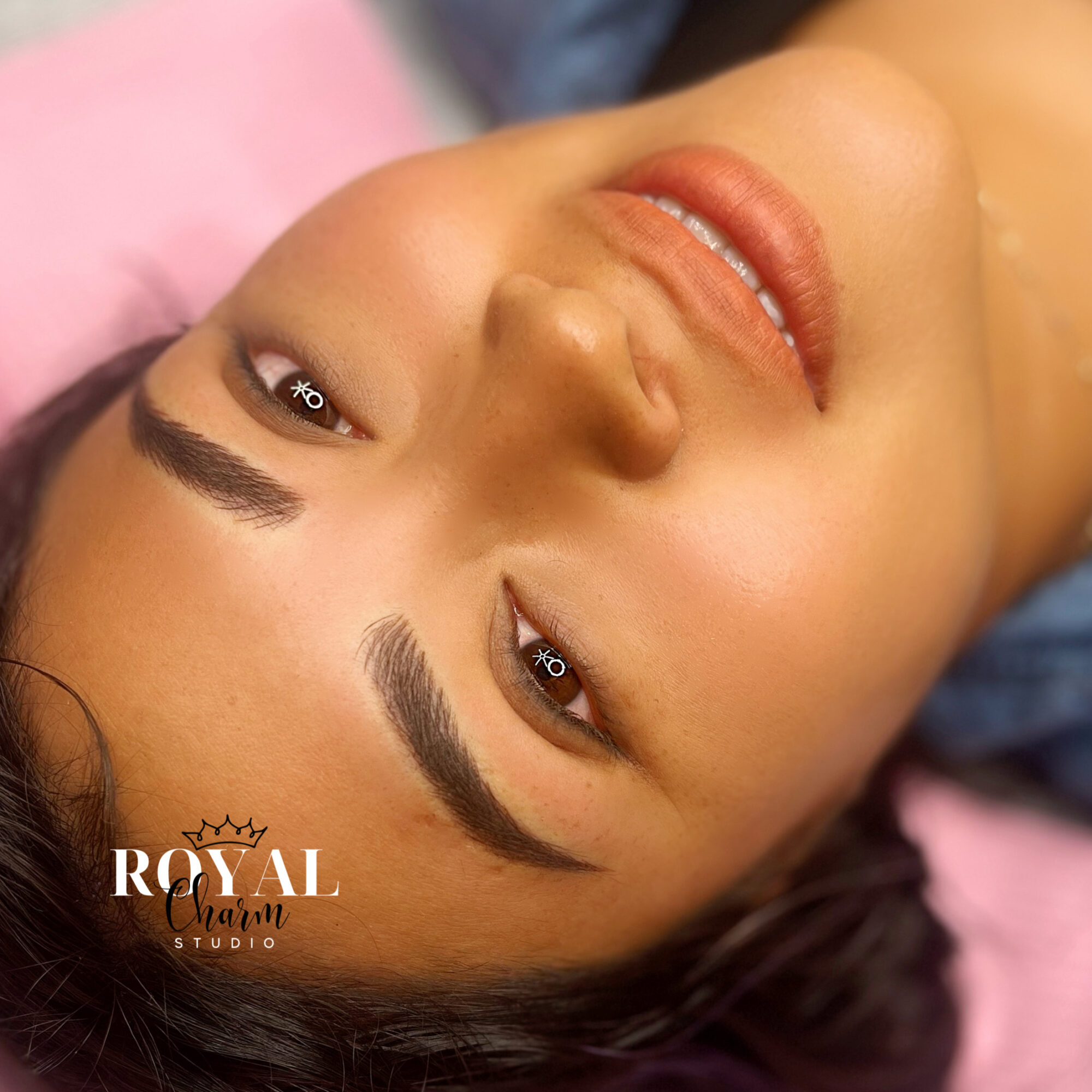 Close-up of a woman's face with makeup, lying down with eyes open and a slight smile.