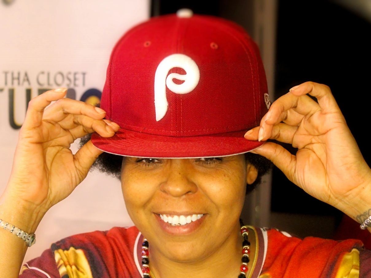 Person wearing a red cap with a white logo, smiling, holding the cap's brim with both hands.