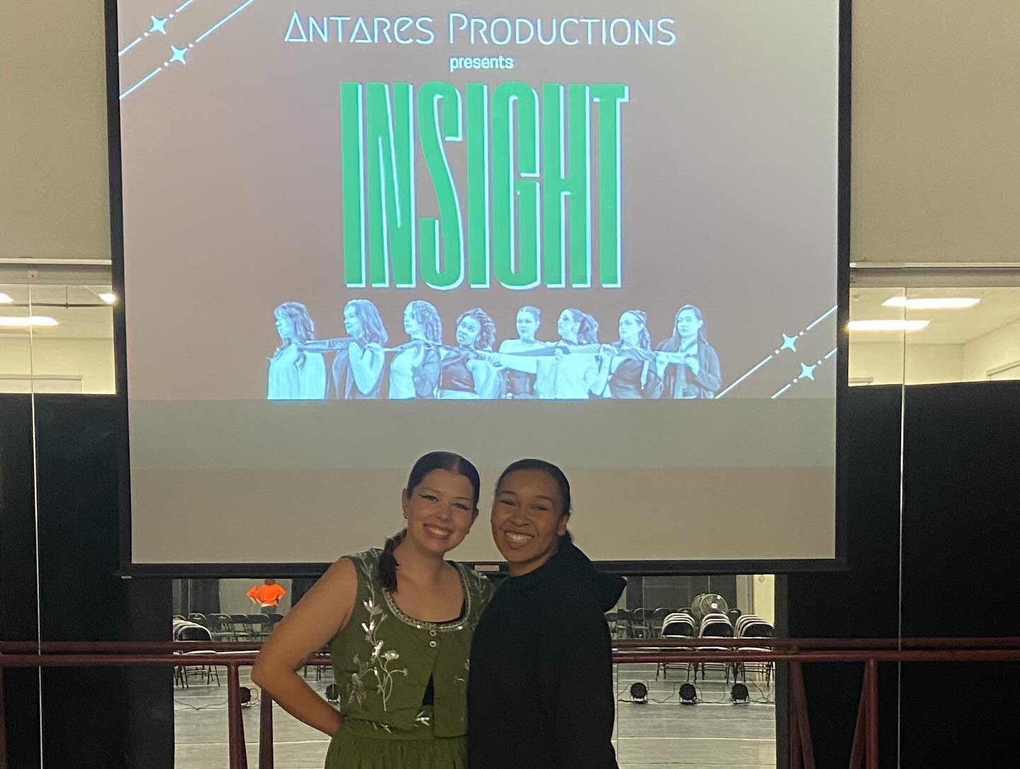Two women stand in front of a large screen displaying the word 'INSIGHT' and a group of people.