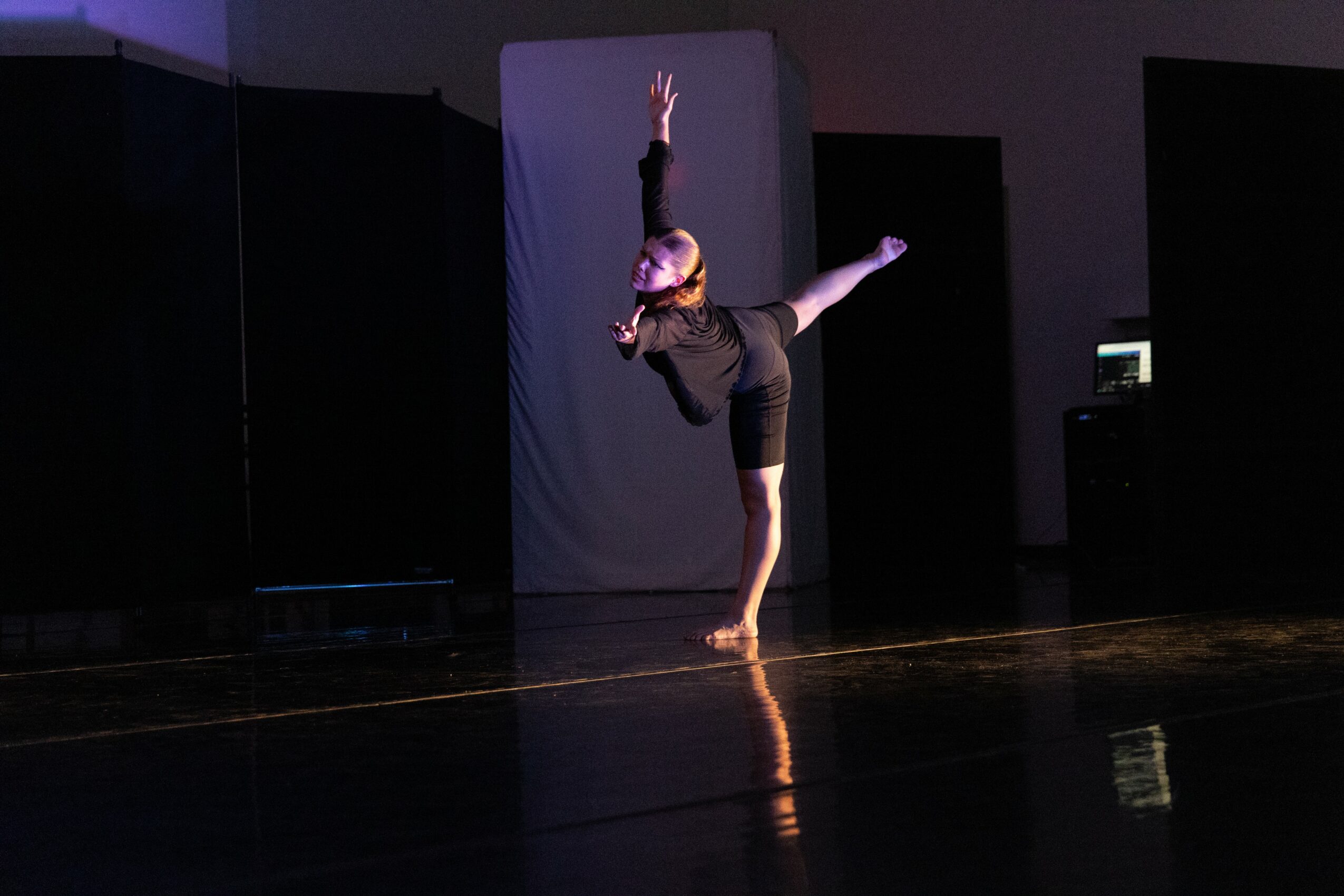 Performer in black outfit balancing on one hand with one leg extended sideways on stage.