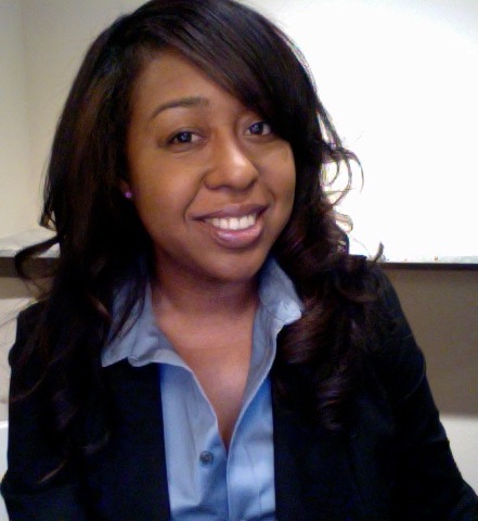 Woman with dark hair smiling, wearing a blue shirt and dark blazer, in an indoor setting.