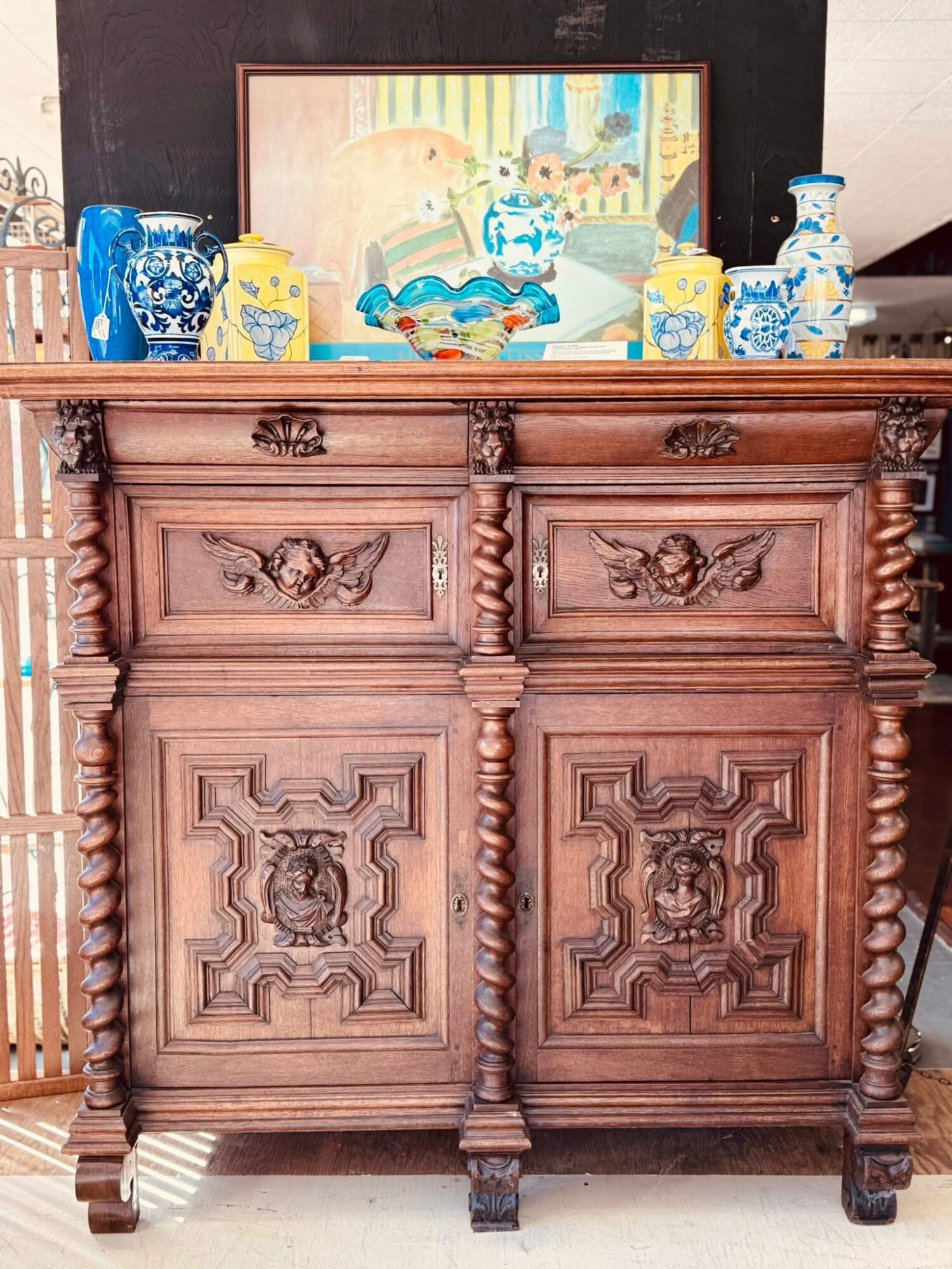 Wooden cabinet with decorative carvings, topped with blue and white porcelain vases and a framed painting in the background.