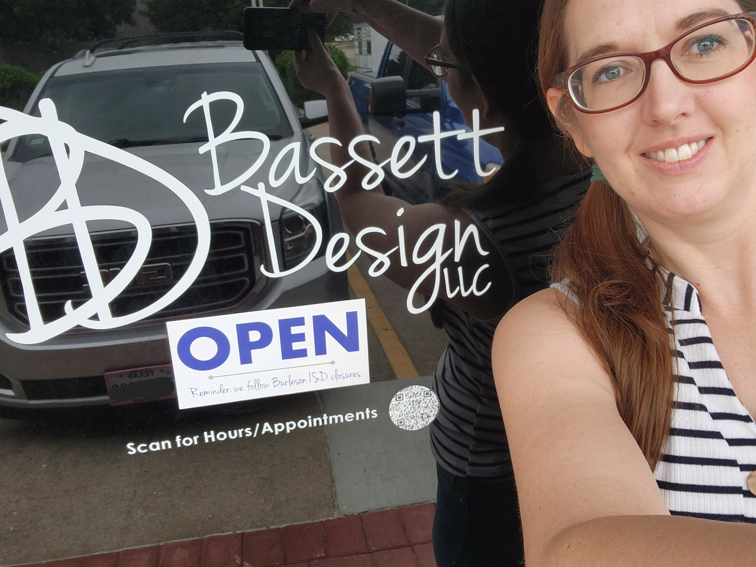 Woman with glasses and striped shirt smiling outside a business with an open sign.