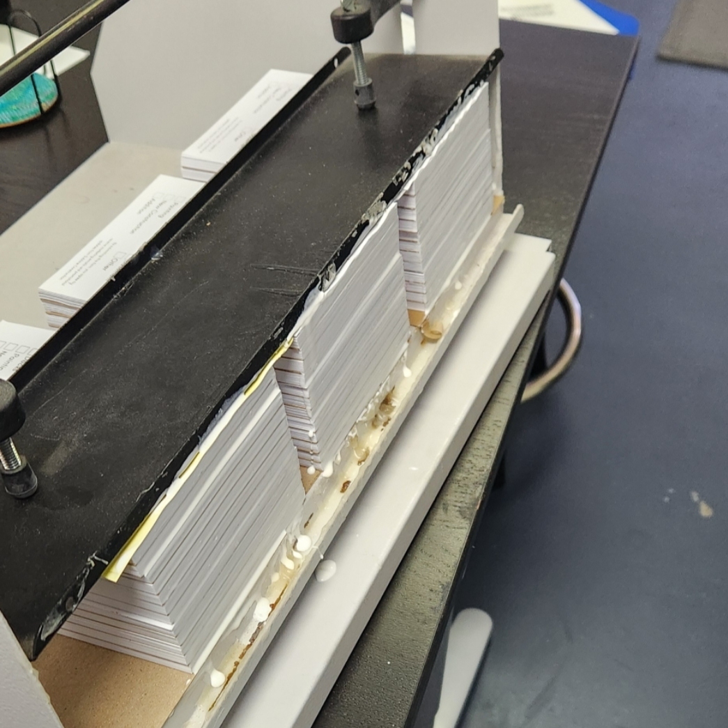 Stack of white paper or cards on a black surface with a metal clamp, on a white tray, in a workspace.