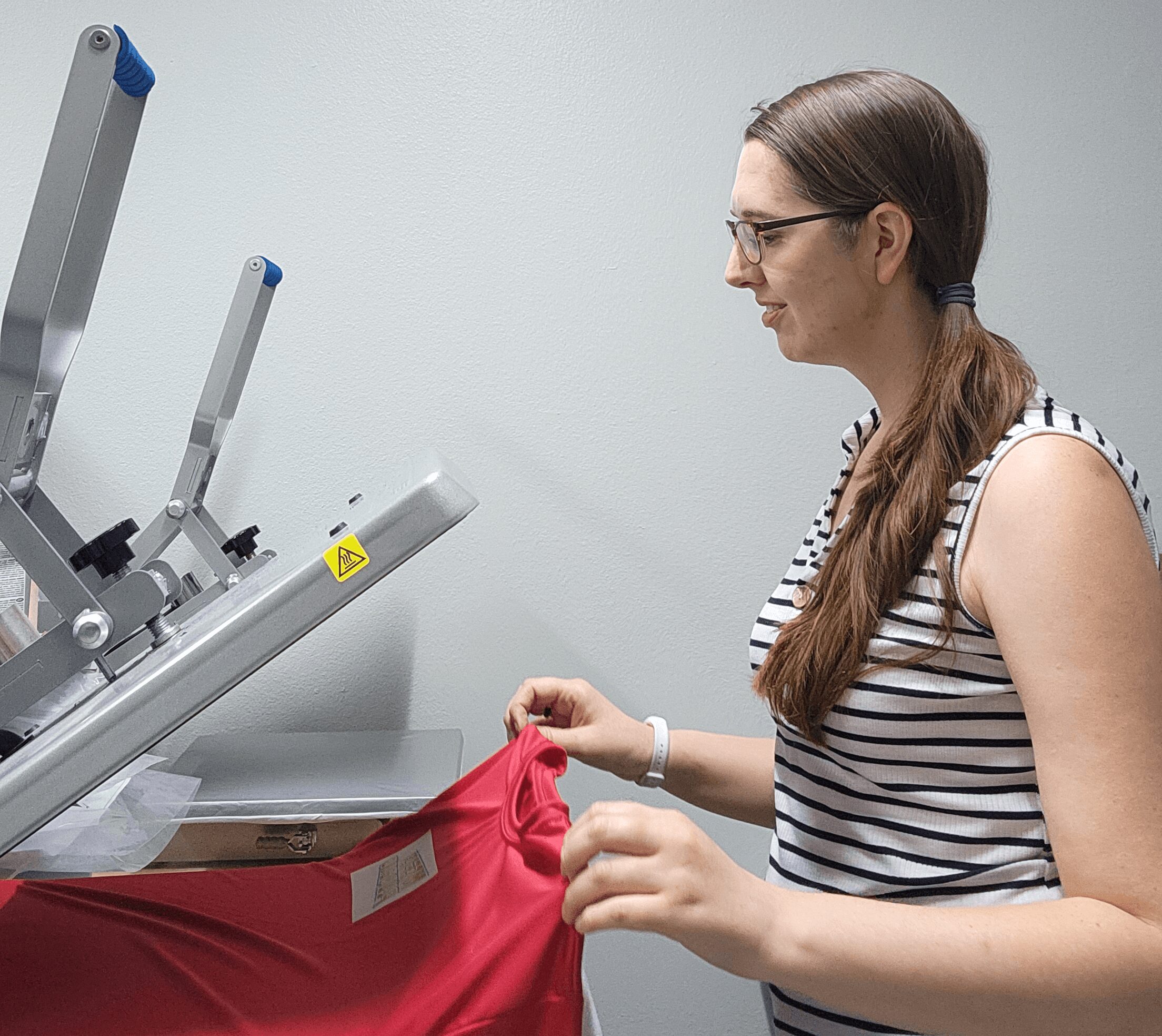 Woman with glasses and long hair using a machine to print on a red fabric.