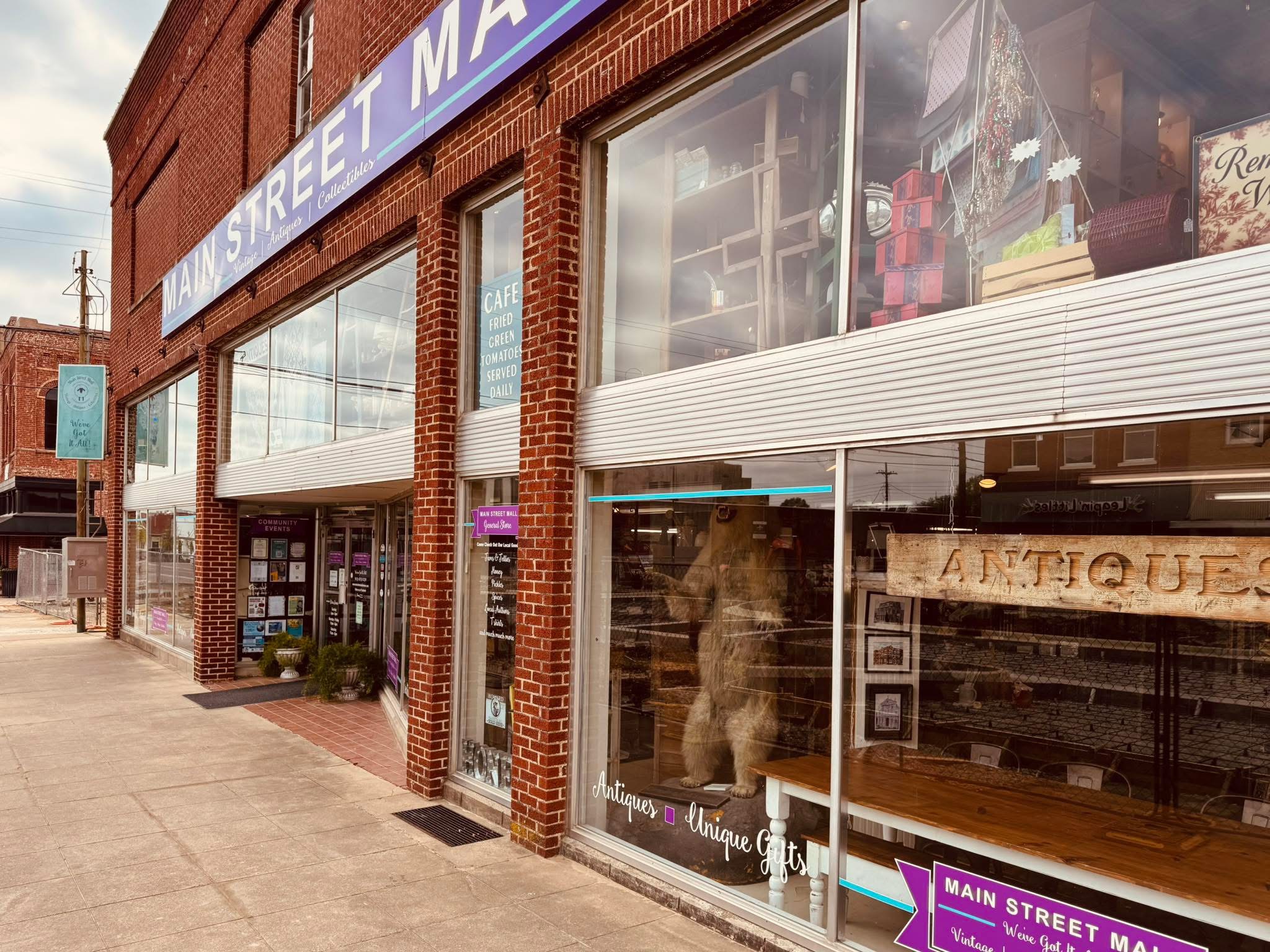 Storefront with large glass windows and brick exterior, displaying books and items inside, on a city sidewalk.