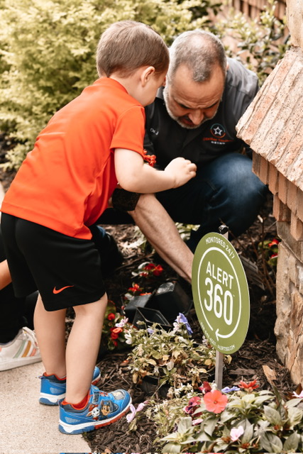 Child and adult looking at flowers near a sign that reads ALERT 360 outdoors.