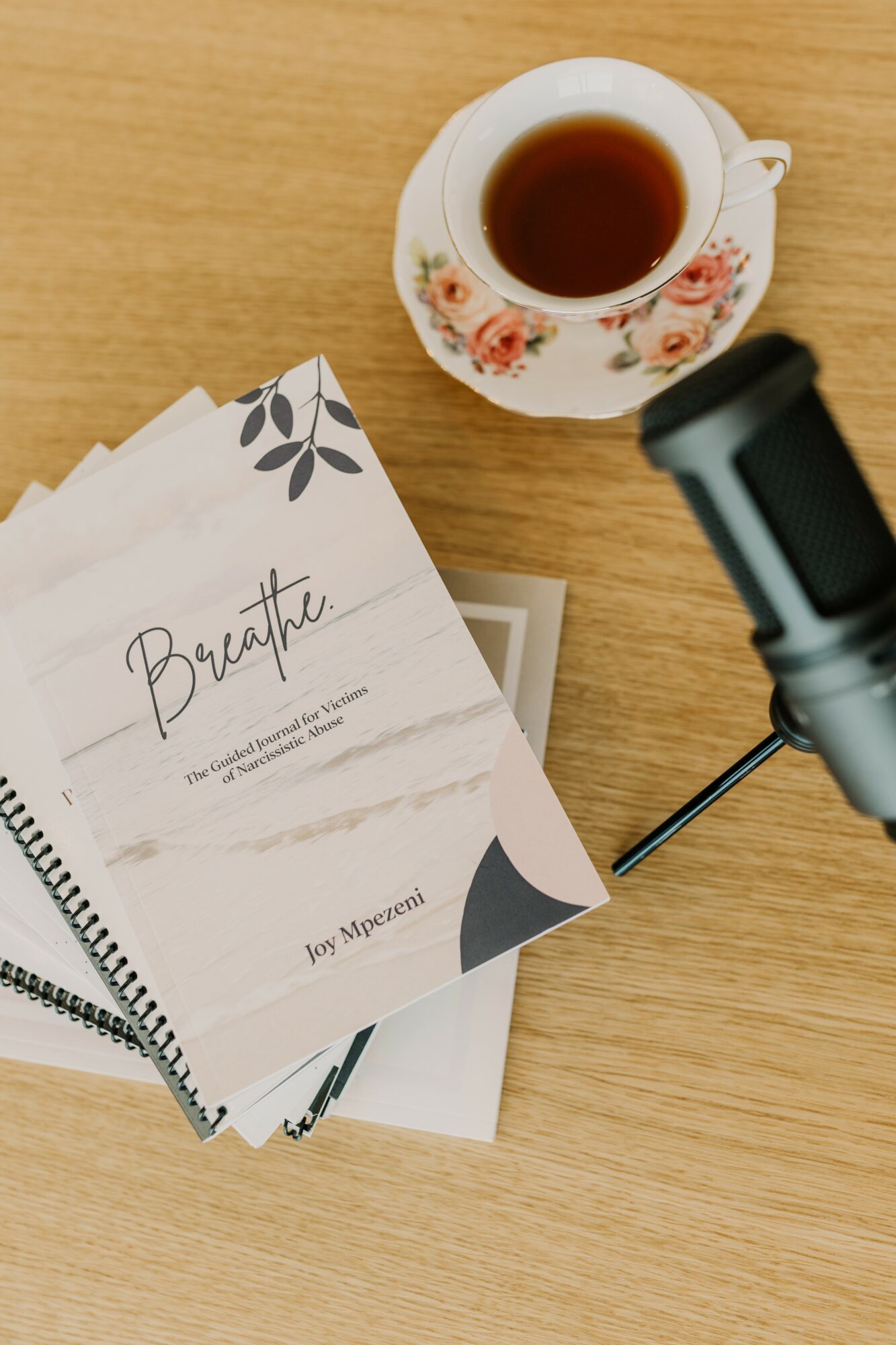Cup of tea or coffee on a floral saucer, papers, and a microphone on a wooden surface.