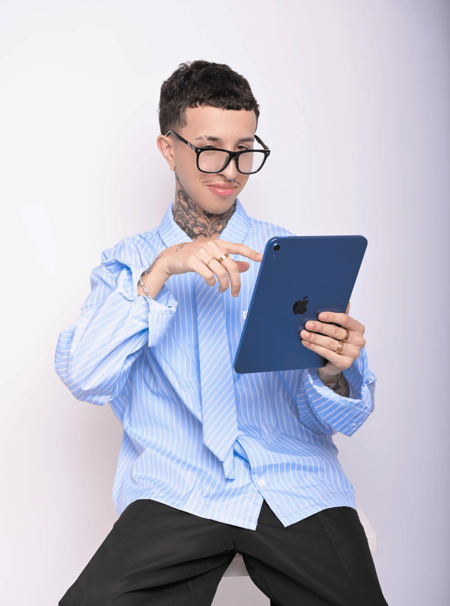 Person with short hair and glasses using a tablet, wearing a blue striped shirt, against a plain background.