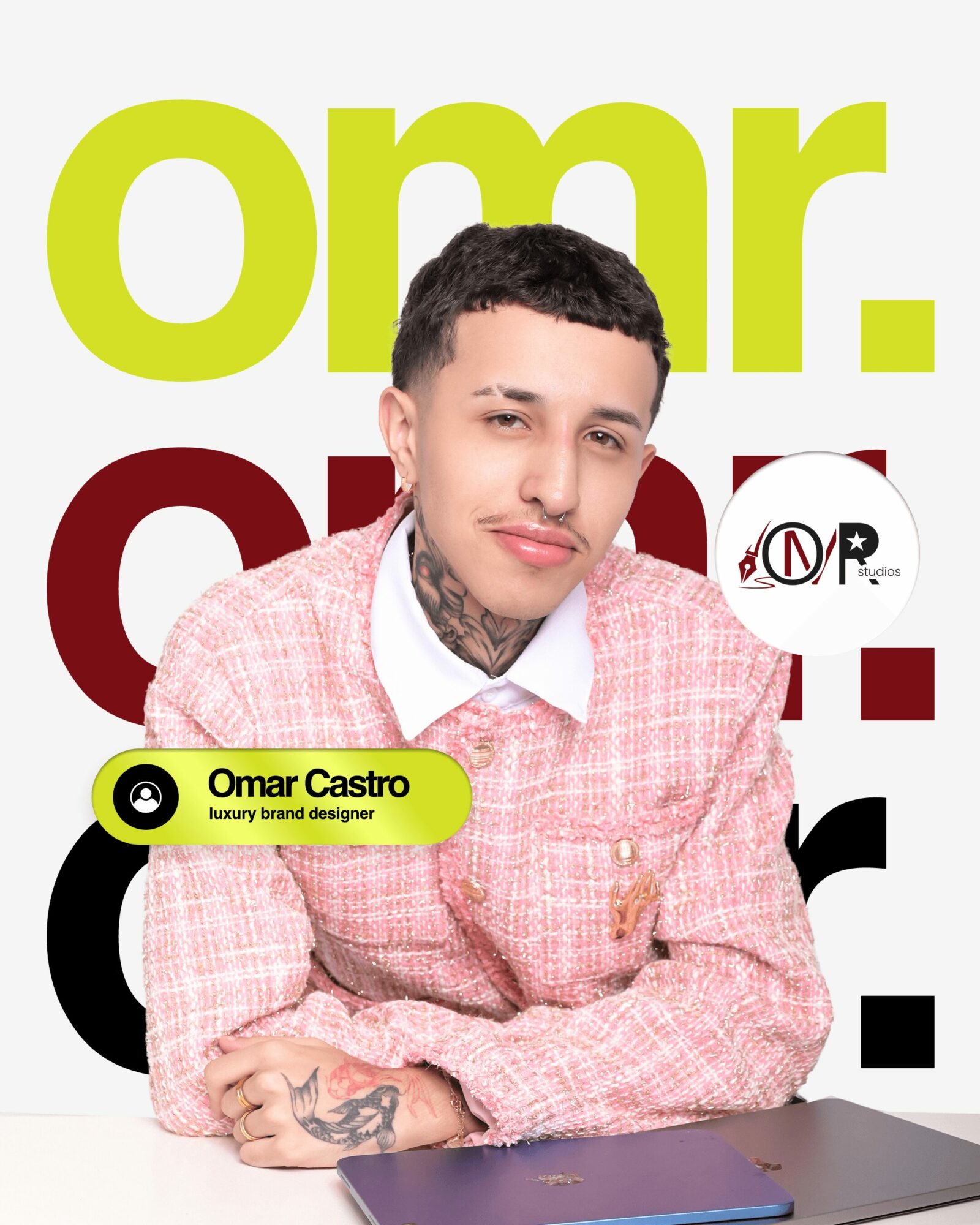 Young man with tattoos wearing pink checkered shirt, sitting at desk with laptop, background with large colorful text.