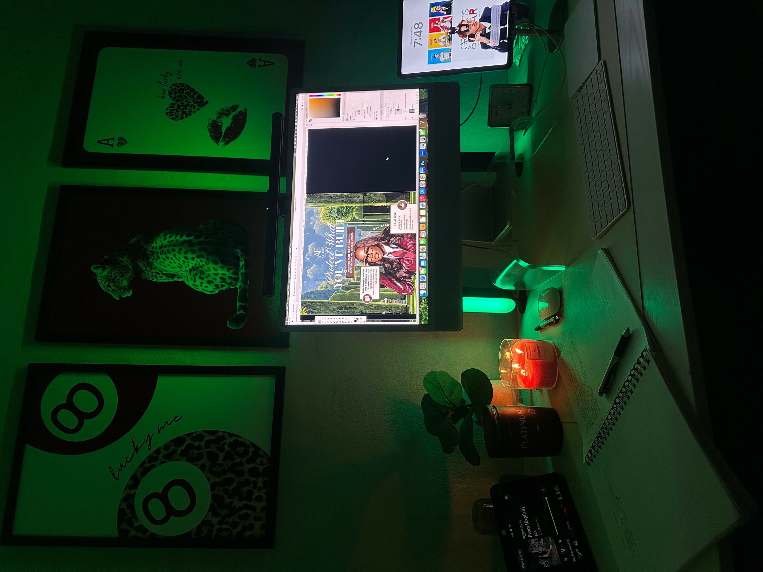 Computer monitor displaying a webpage, surrounded by framed artwork and a desk with a lamp and bottles.