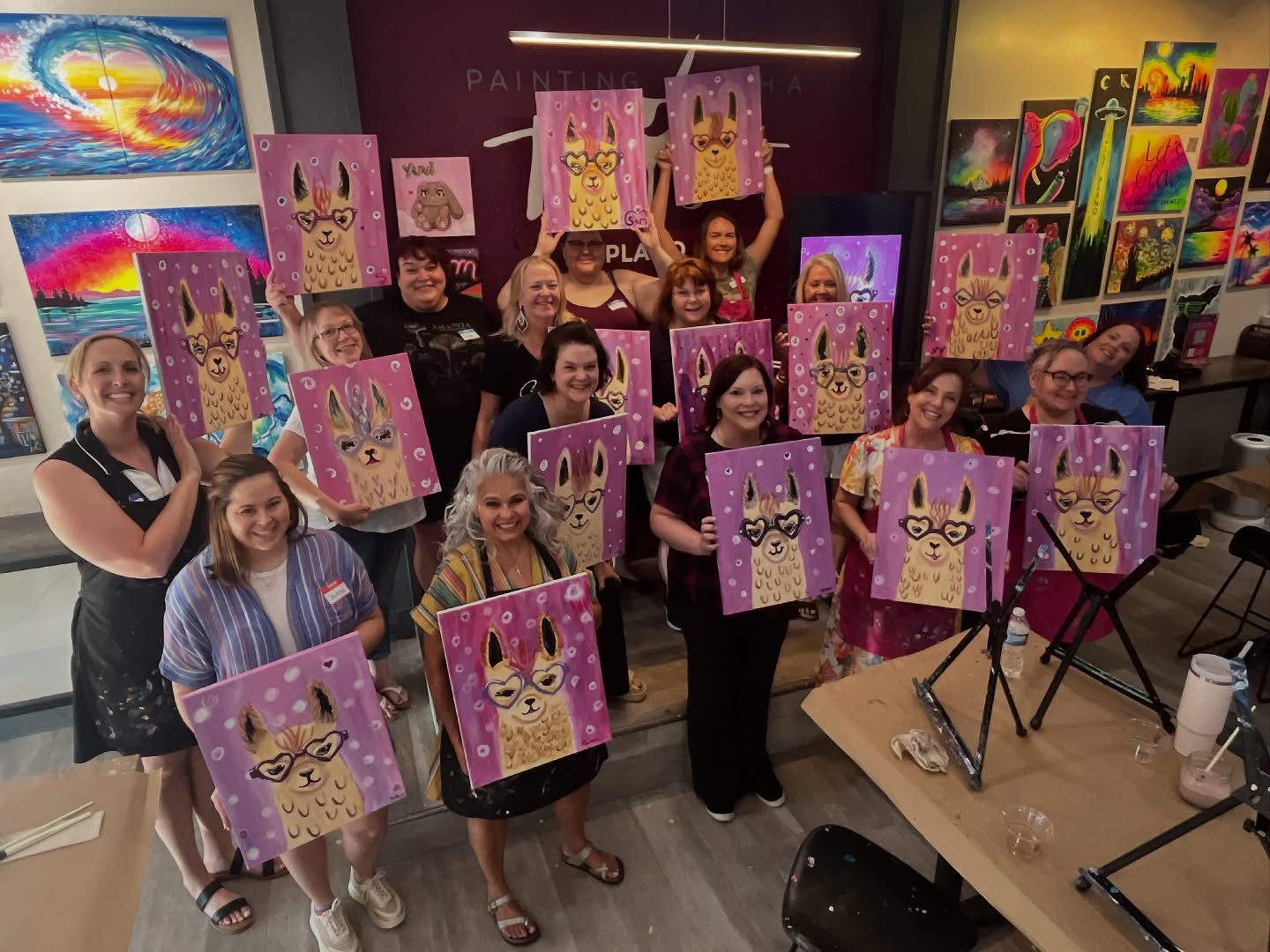 Group of people holding colorful paintings of cats with glasses and crowns in an art gallery.