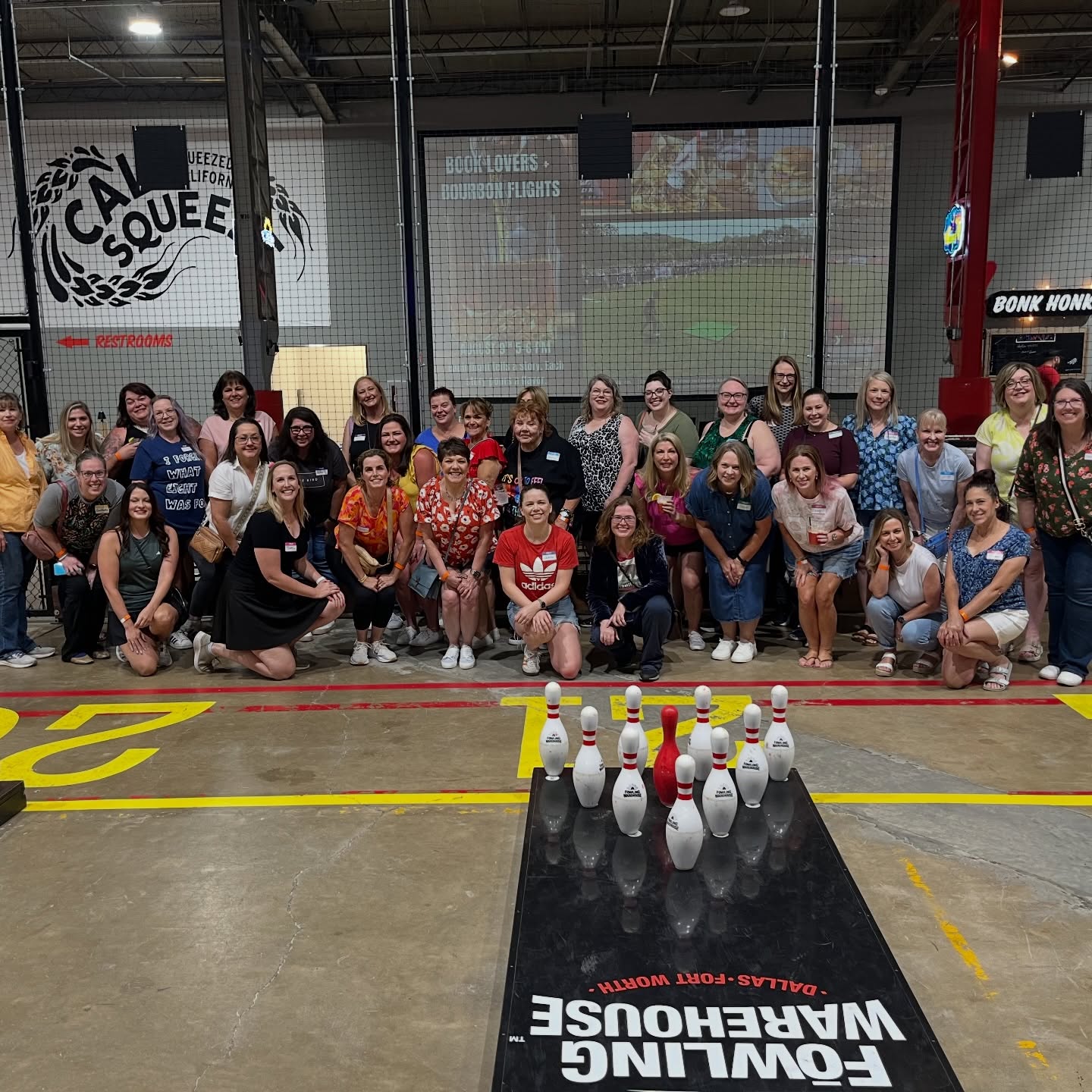 Group of people posing behind bowling pins on a black lane in an indoor bowling alley.
