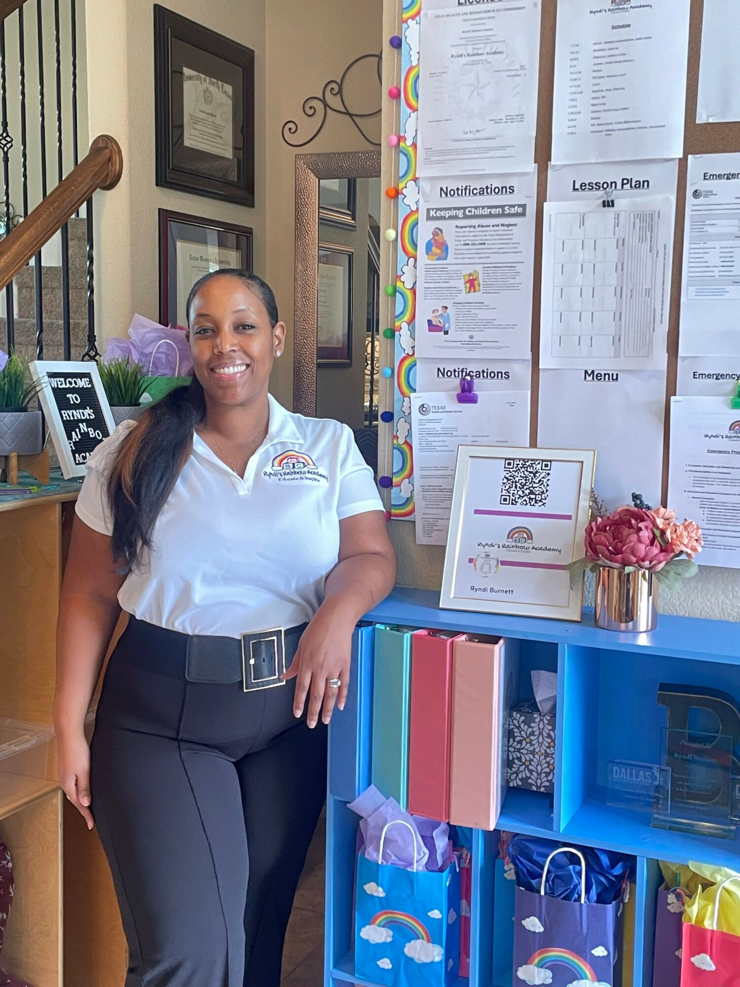 Smiling woman in uniform standing indoors near colorful shelves and bulletin board with papers and notices.