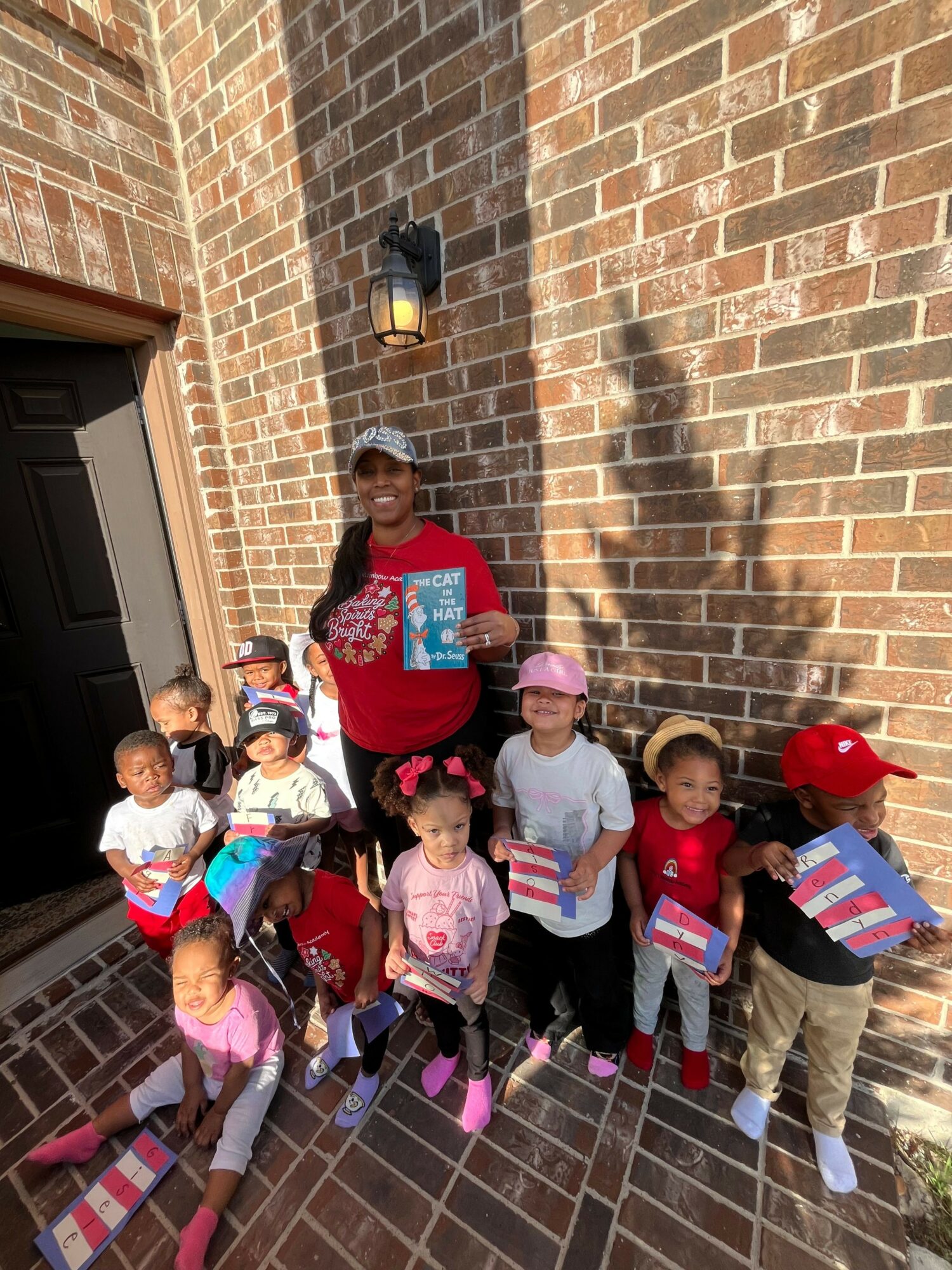 Group of children and an adult standing outside on brick patio, holding gift bags and boxes, with brick wall background.