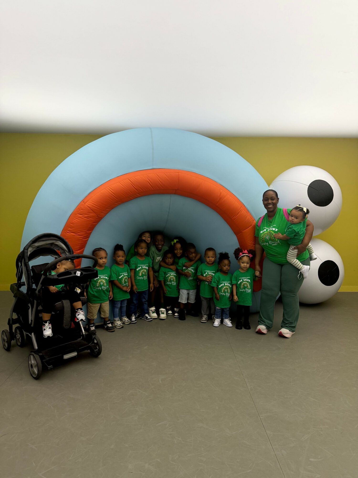 Group of children and an adult standing in front of a large inflatable structure with a blue arch and white spheres, indoors.