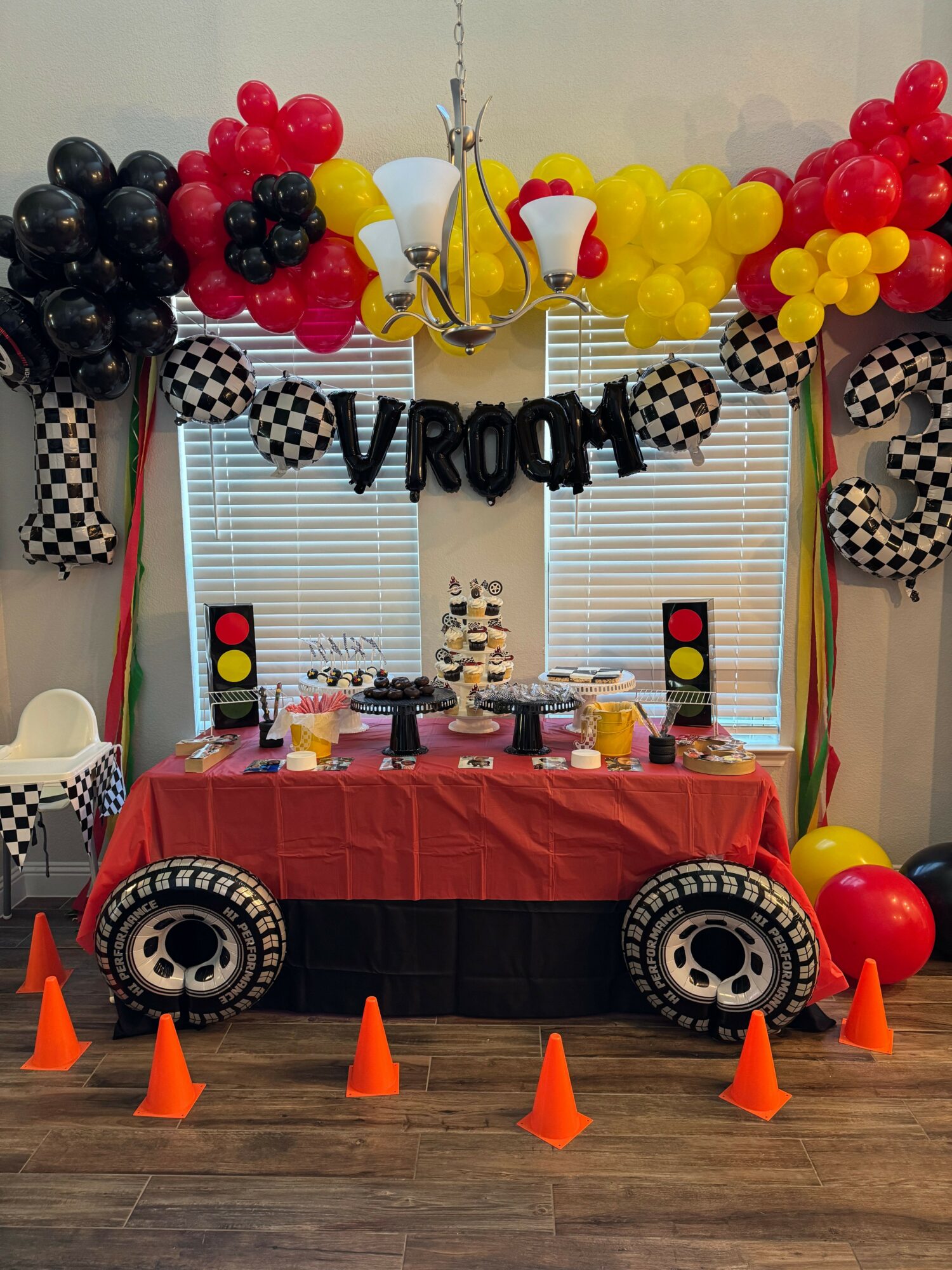 Party setup with checkered and balloon decorations, a table with treats, and traffic cone decorations in front.