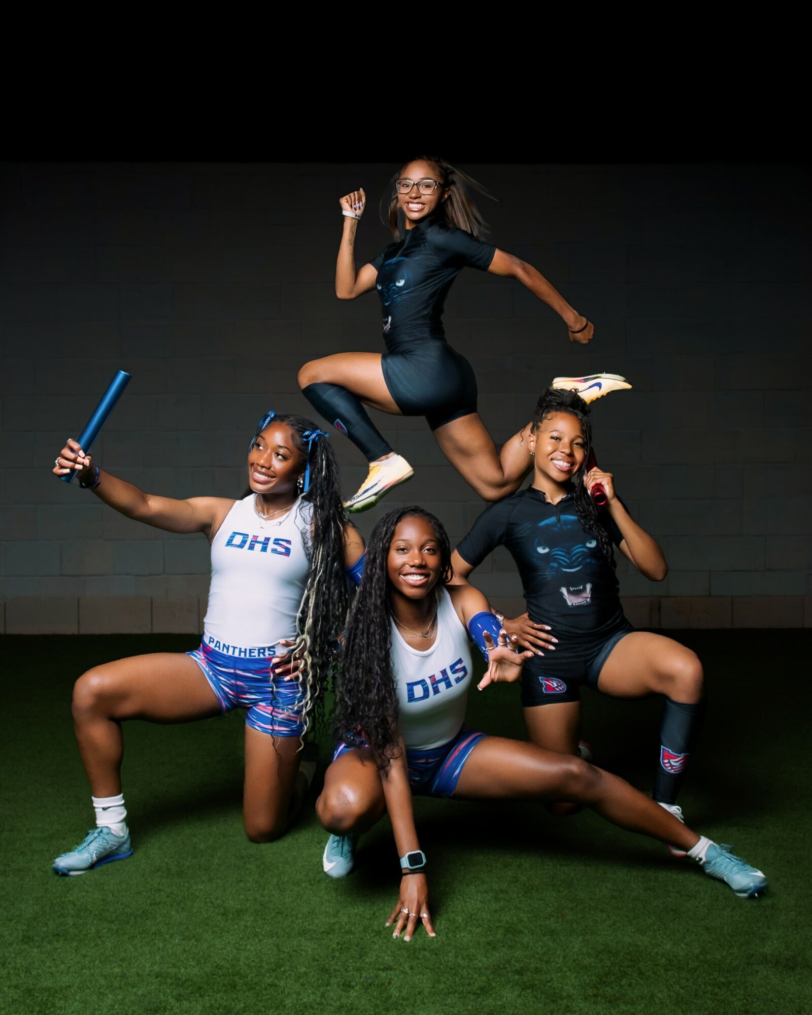 Four young women in athletic outfits pose dynamically indoors against a dark background, smiling and holding sports equipment.
