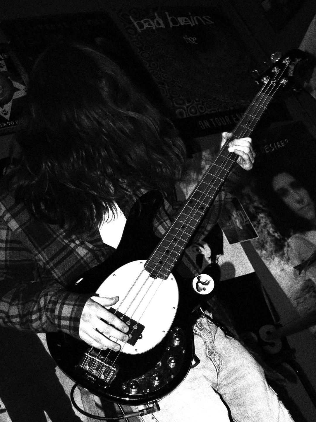 Person with long hair playing a black and white electric bass guitar indoors.
