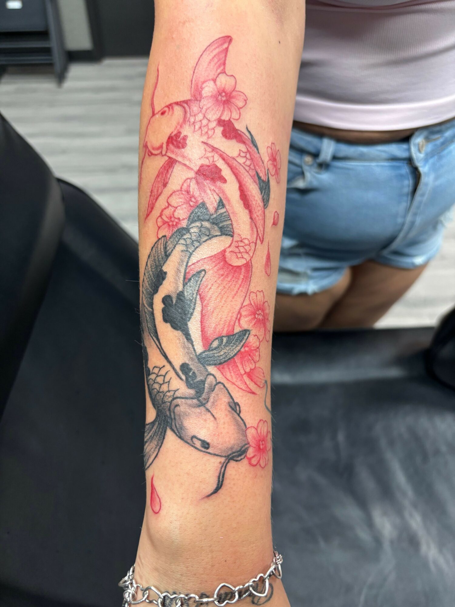 Forearm tattoo of a dolphin jumping over water with pink flowers and waves, in red, blue, and black ink.