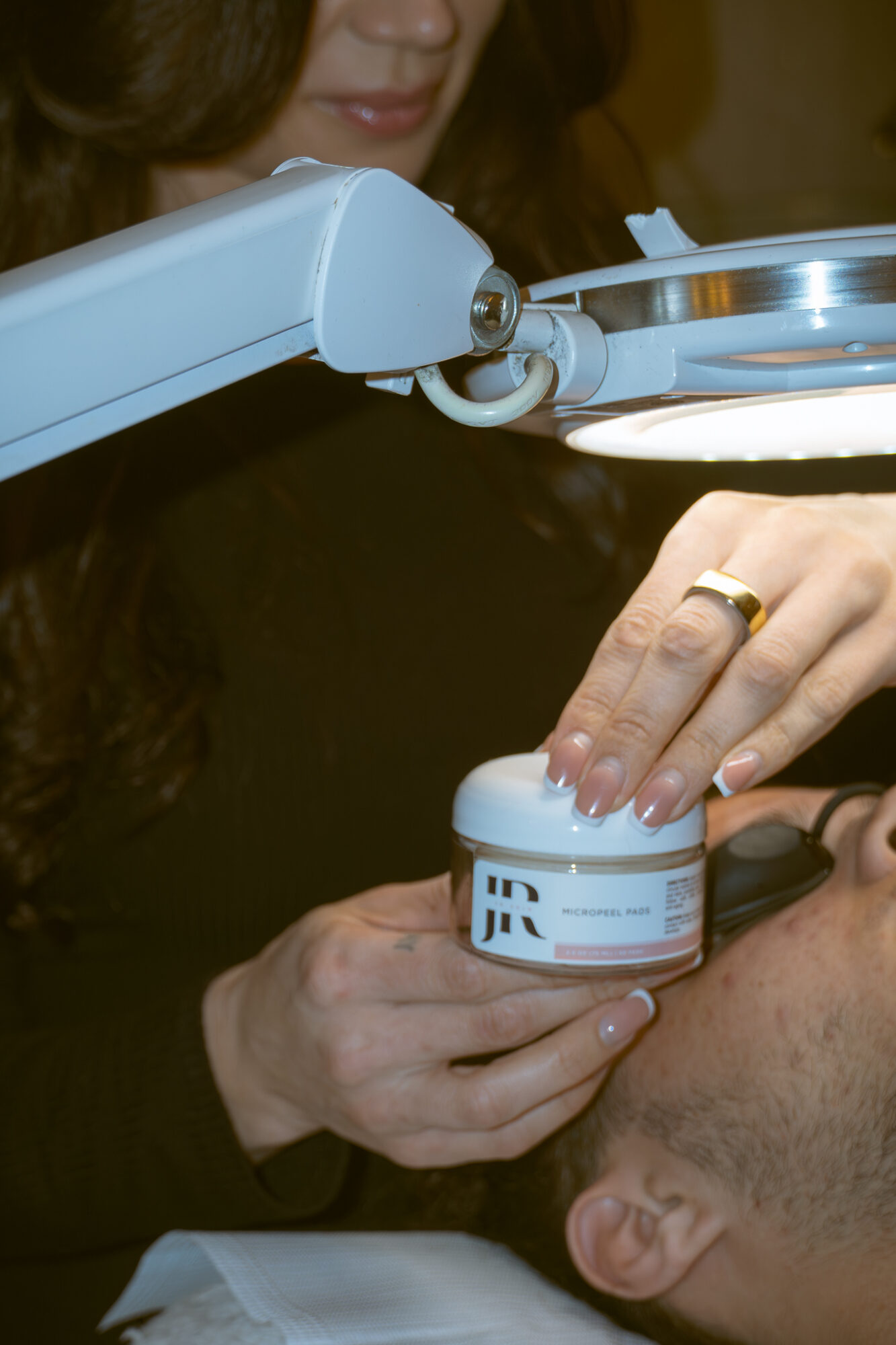 Person holding a small jar near another person's face in a clinical setting.