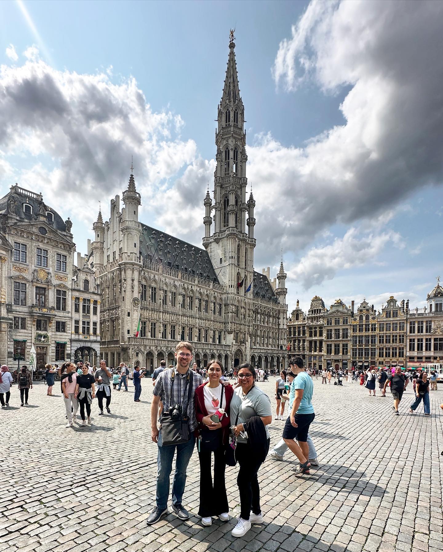 Four people standing in a large open square with historic buildings and a tall church tower behind them.