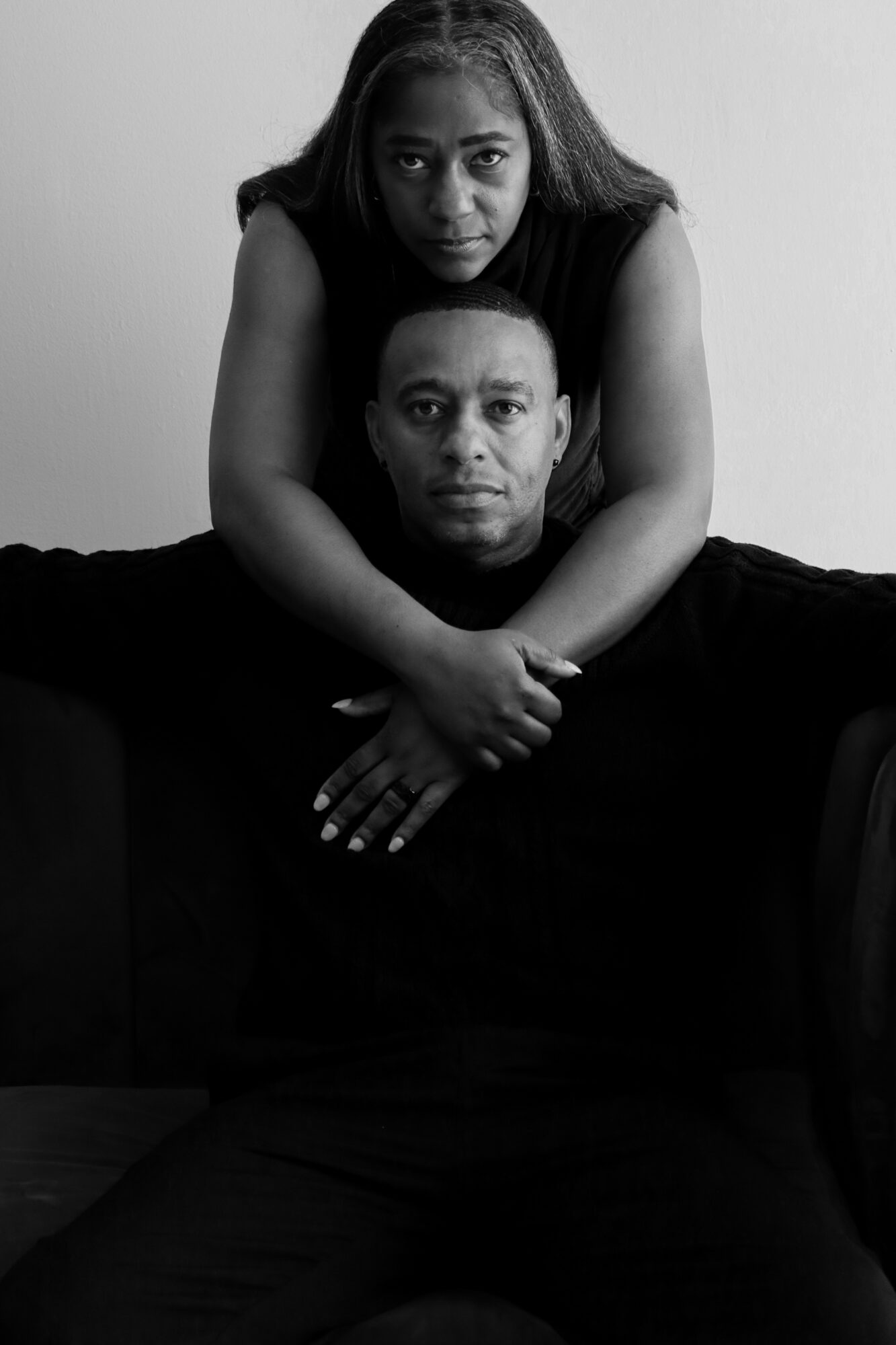 Two people, one sitting and one leaning on their shoulders, in a black and white portrait.