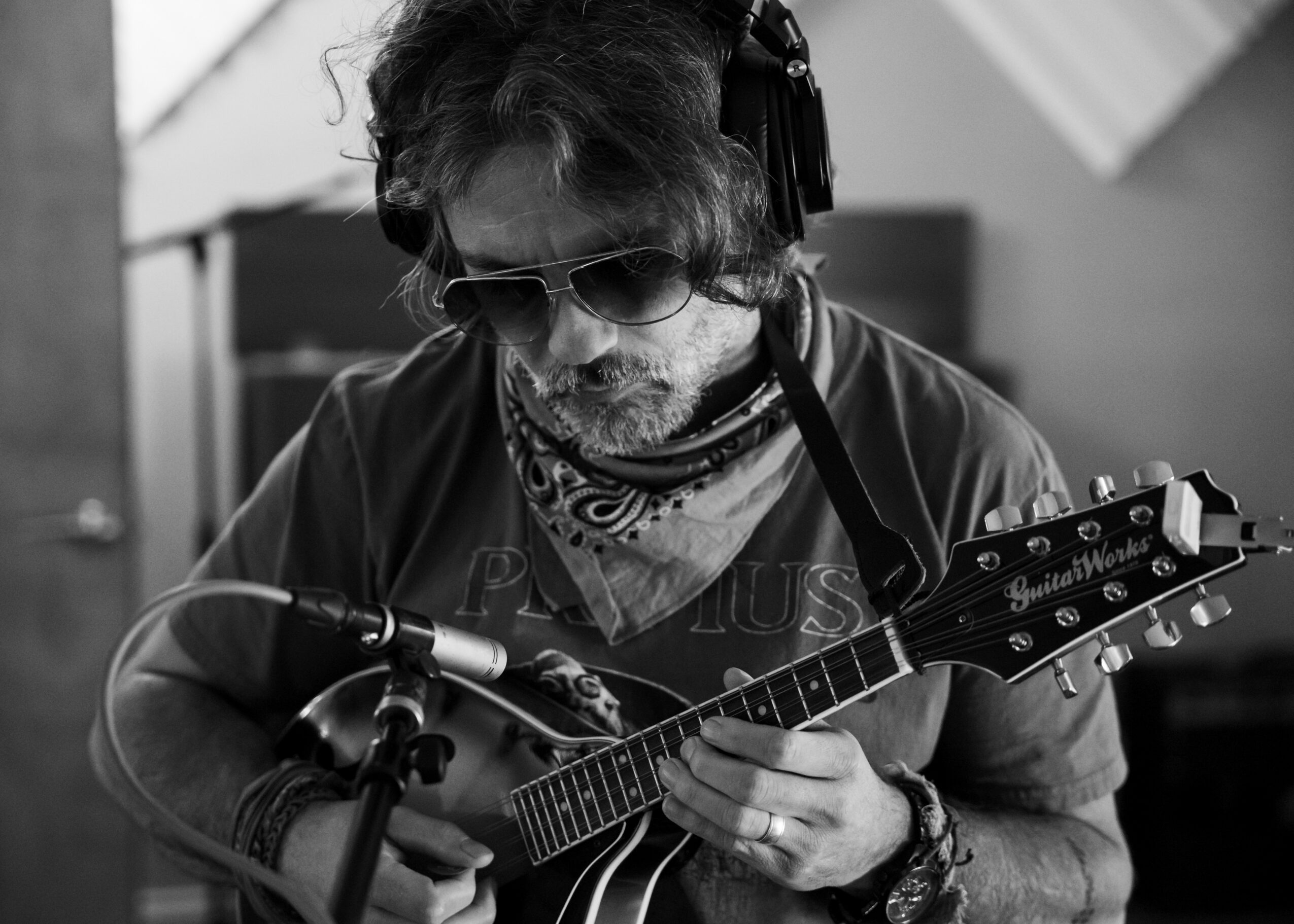 Person with sunglasses and headphones playing a guitar in a recording studio.