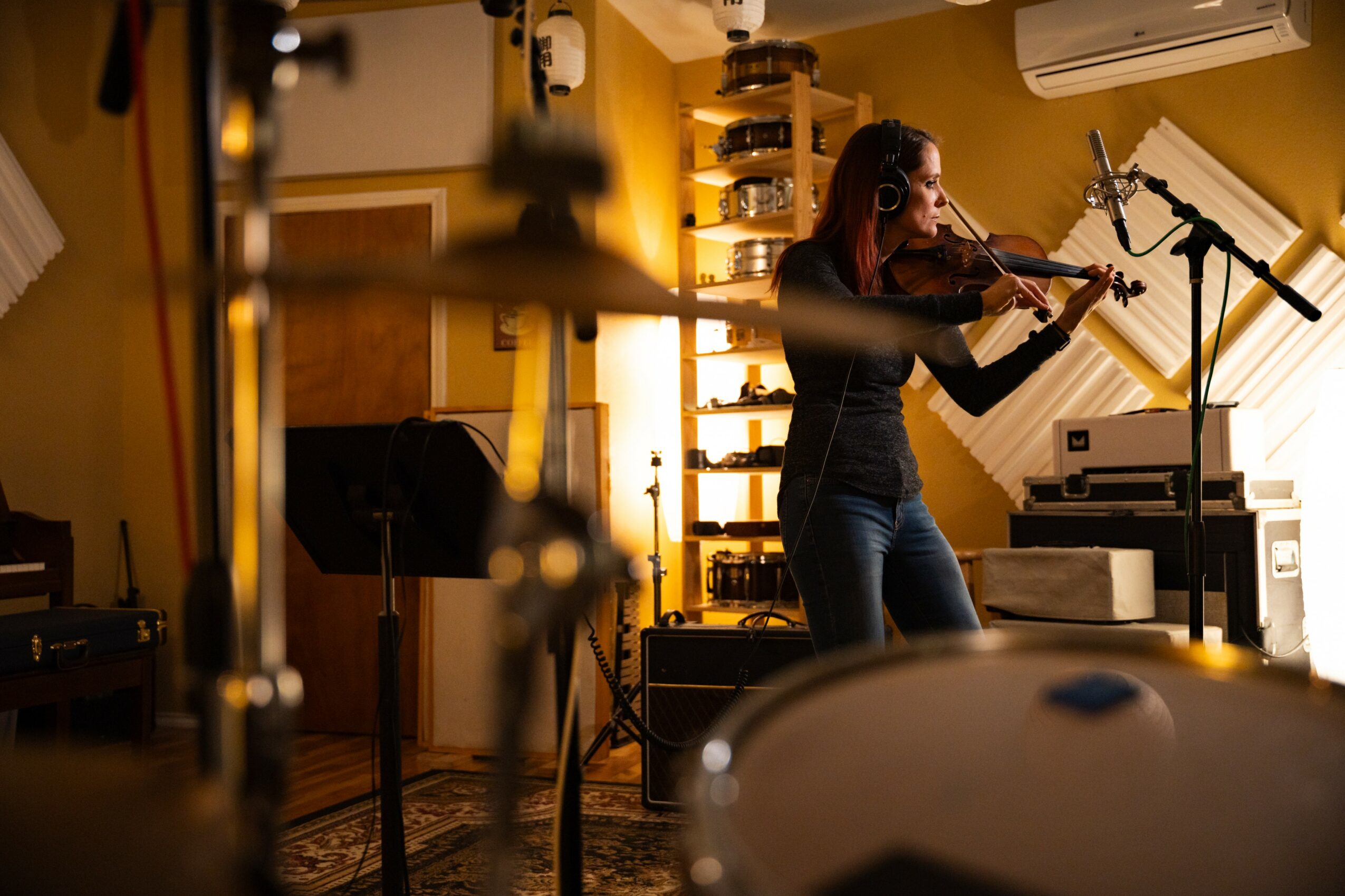 Woman playing violin in a music studio with musical instruments and equipment around her.