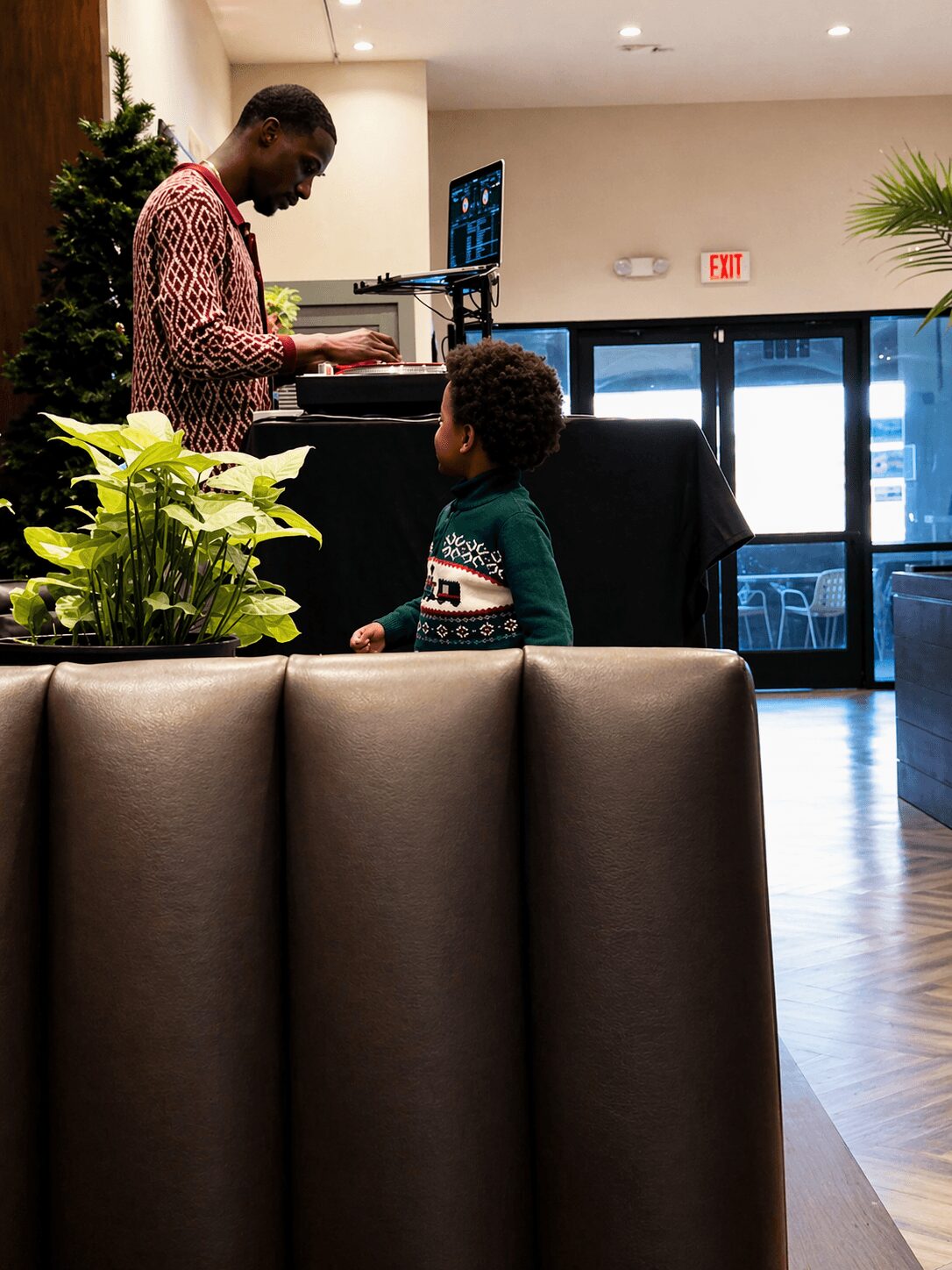 Adult and child standing near a table with plants, inside a room with large windows and a Christmas tree.