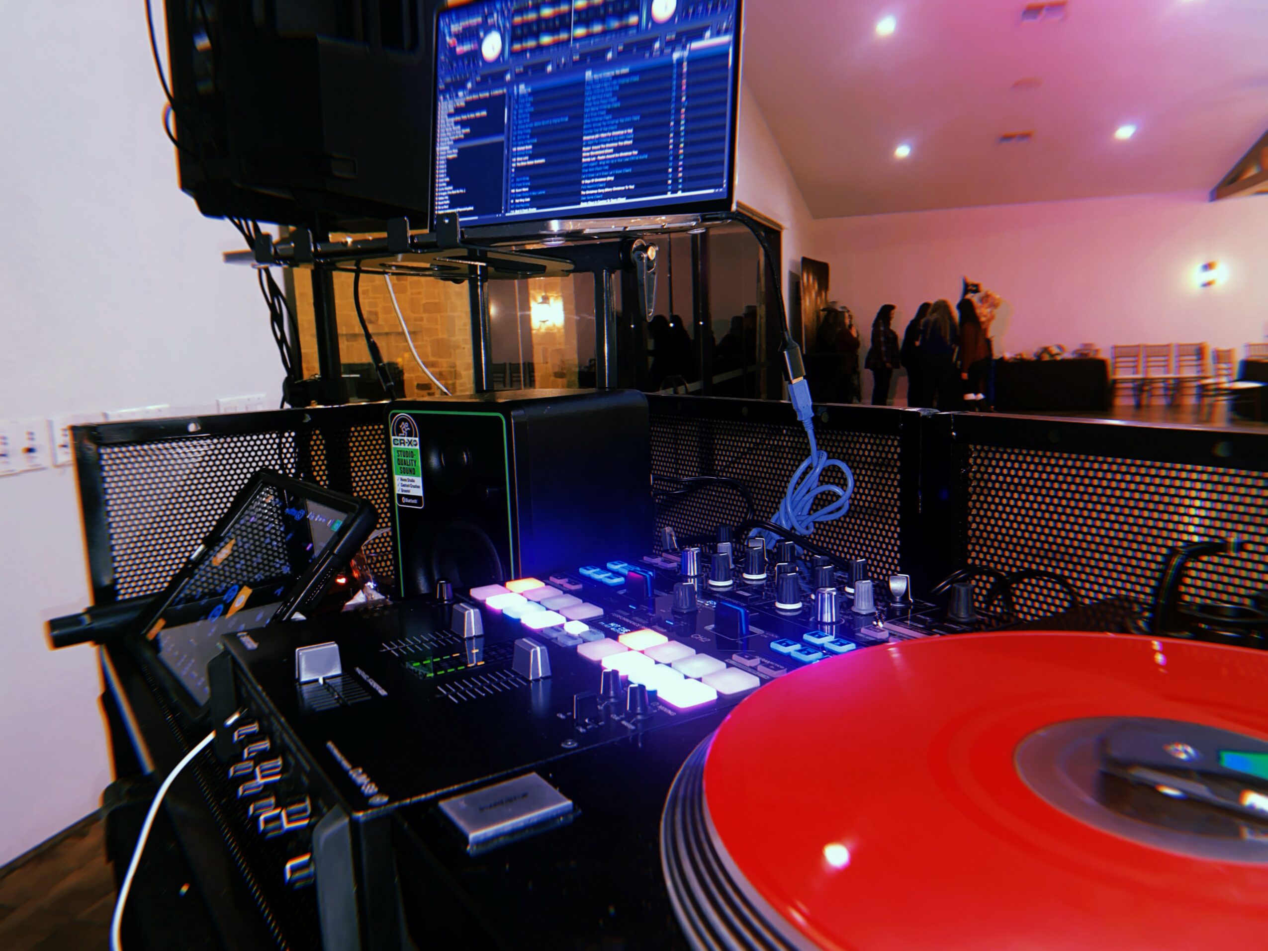DJ equipment with turntable, mixer, and laptop in a room with people in the background.