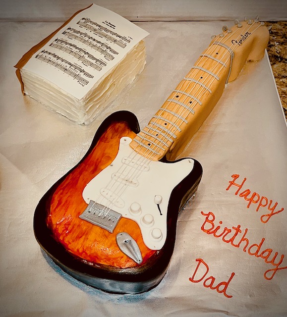 Guitar-shaped cake with sheet music and birthday message for dad.