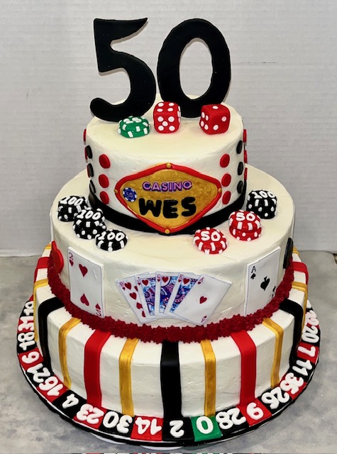 Three-tier cake decorated with casino theme, playing cards, dice, and a large number 50 topper.