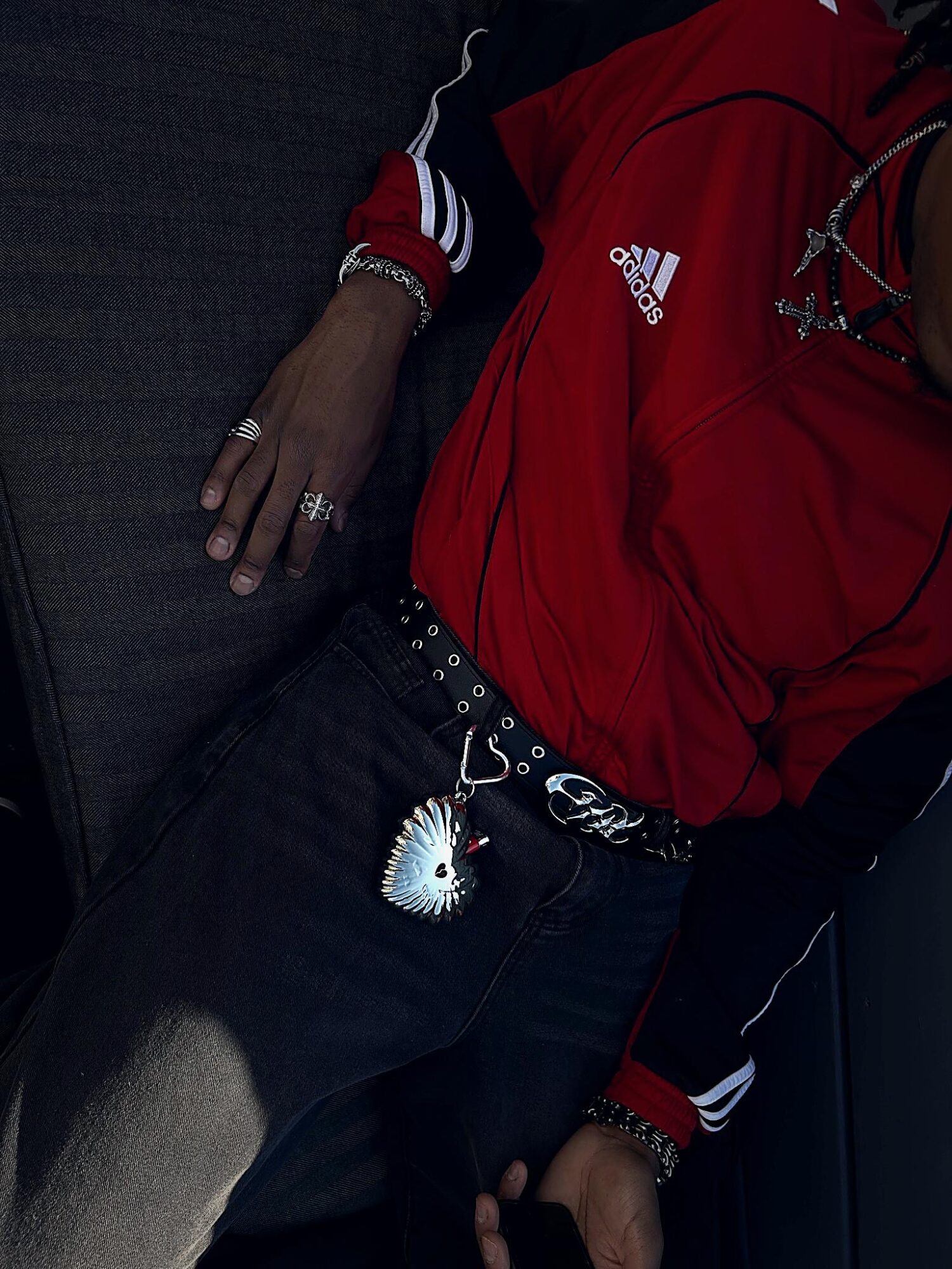 Person wearing a red Adidas shirt, black pants, and jewelry, with a unicorn keychain attached to the belt loop.