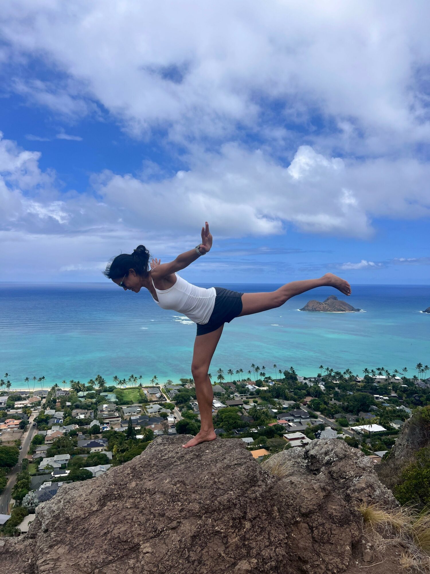 Person performing yoga pose on rock with ocean and sky in background.