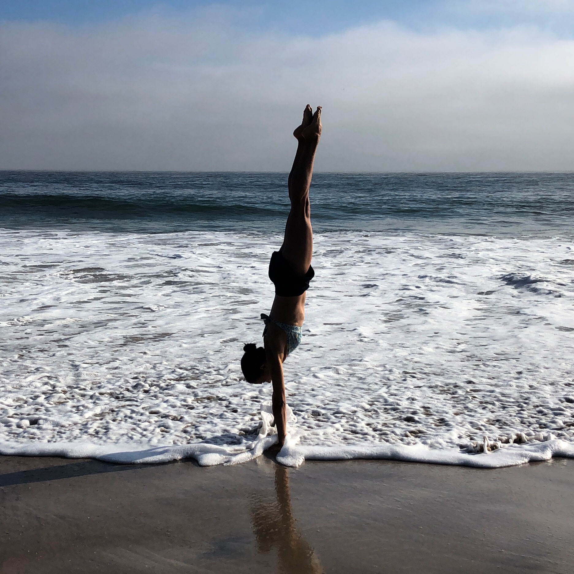 Person performing a handstand on the beach with ocean waves in the background.