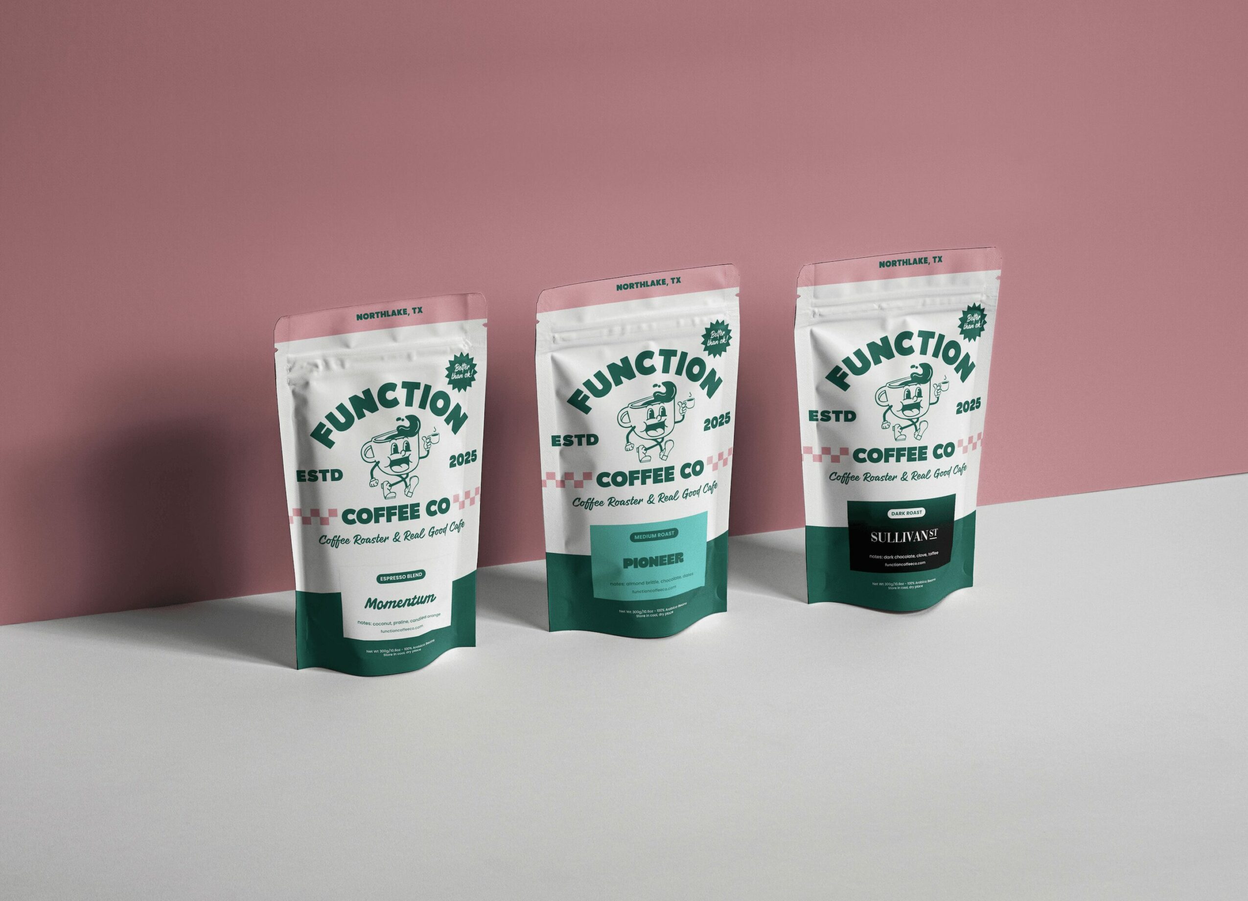 Three standing coffee product packages on a white surface against a pink wall.
