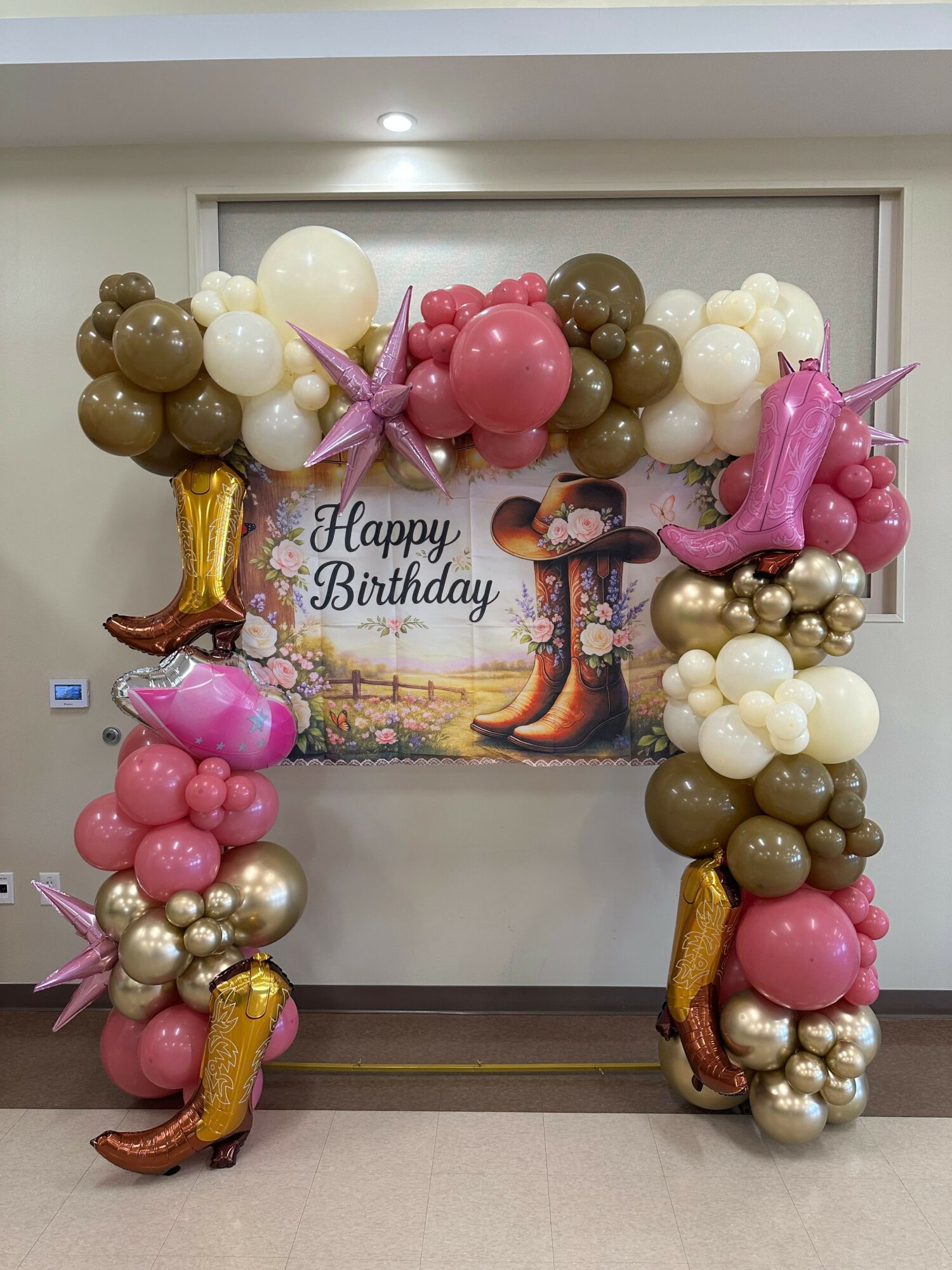 Balloon arch with pink, white, gold, and brown balloons, unicorn and star-shaped balloons, and a birthday sign in the background.