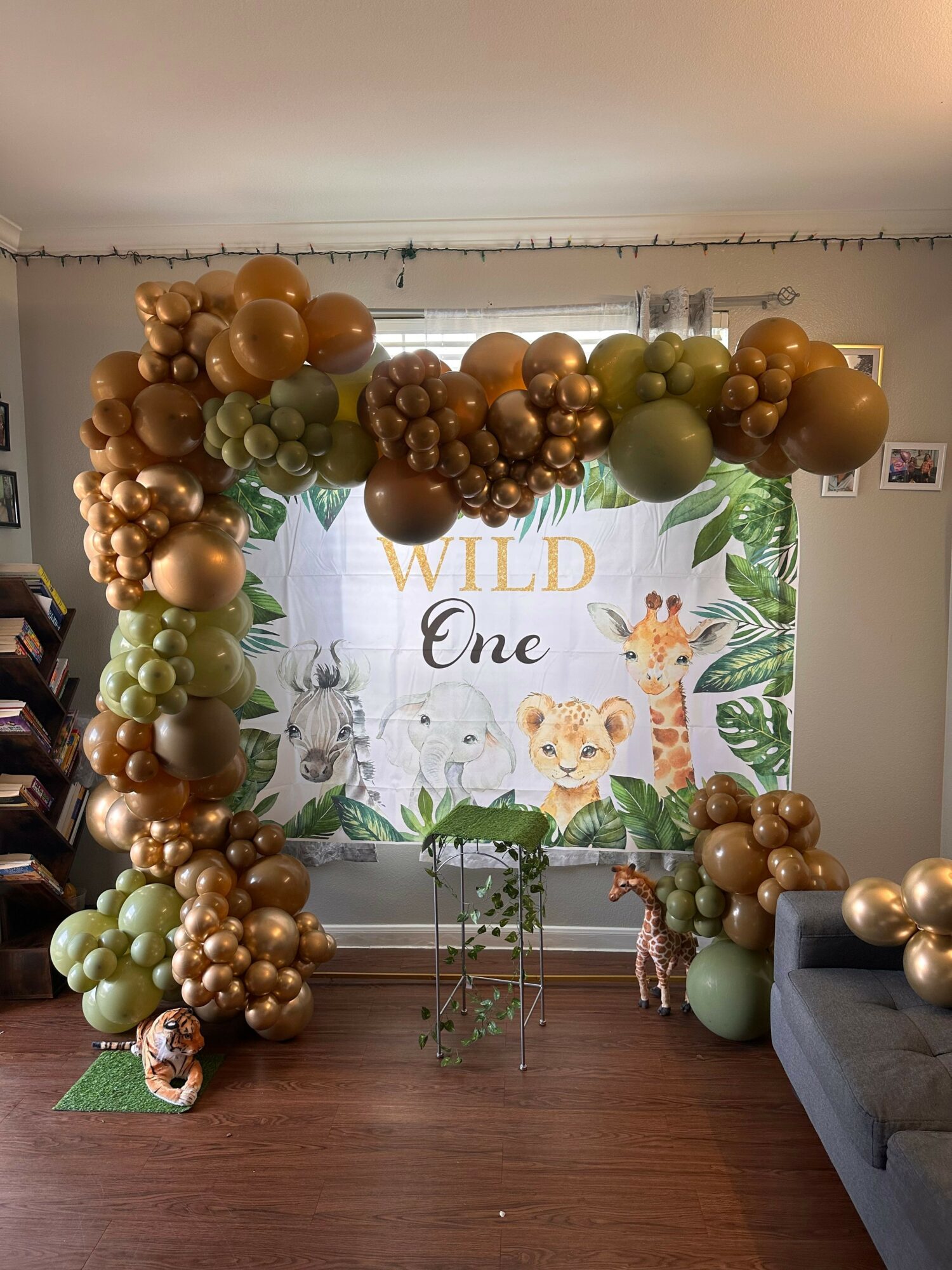 Balloon arch with gold, green, and bronze balloons in front of a jungle-themed backdrop with a lion and giraffe.