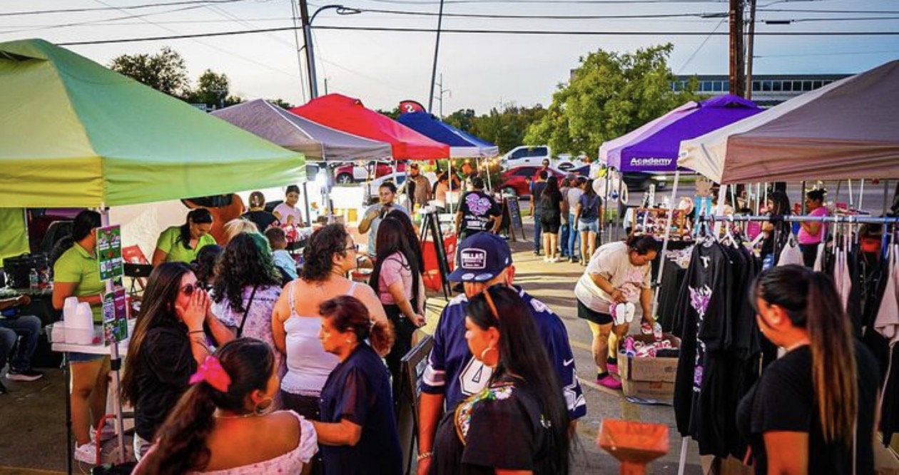 People browsing outdoor market stalls with colorful tents and clothing displays on a sunny day.