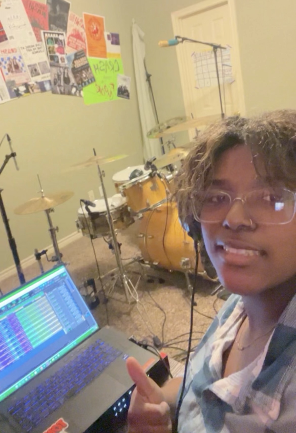 Person with glasses giving a thumbs-up in a room with musical instruments and a laptop.