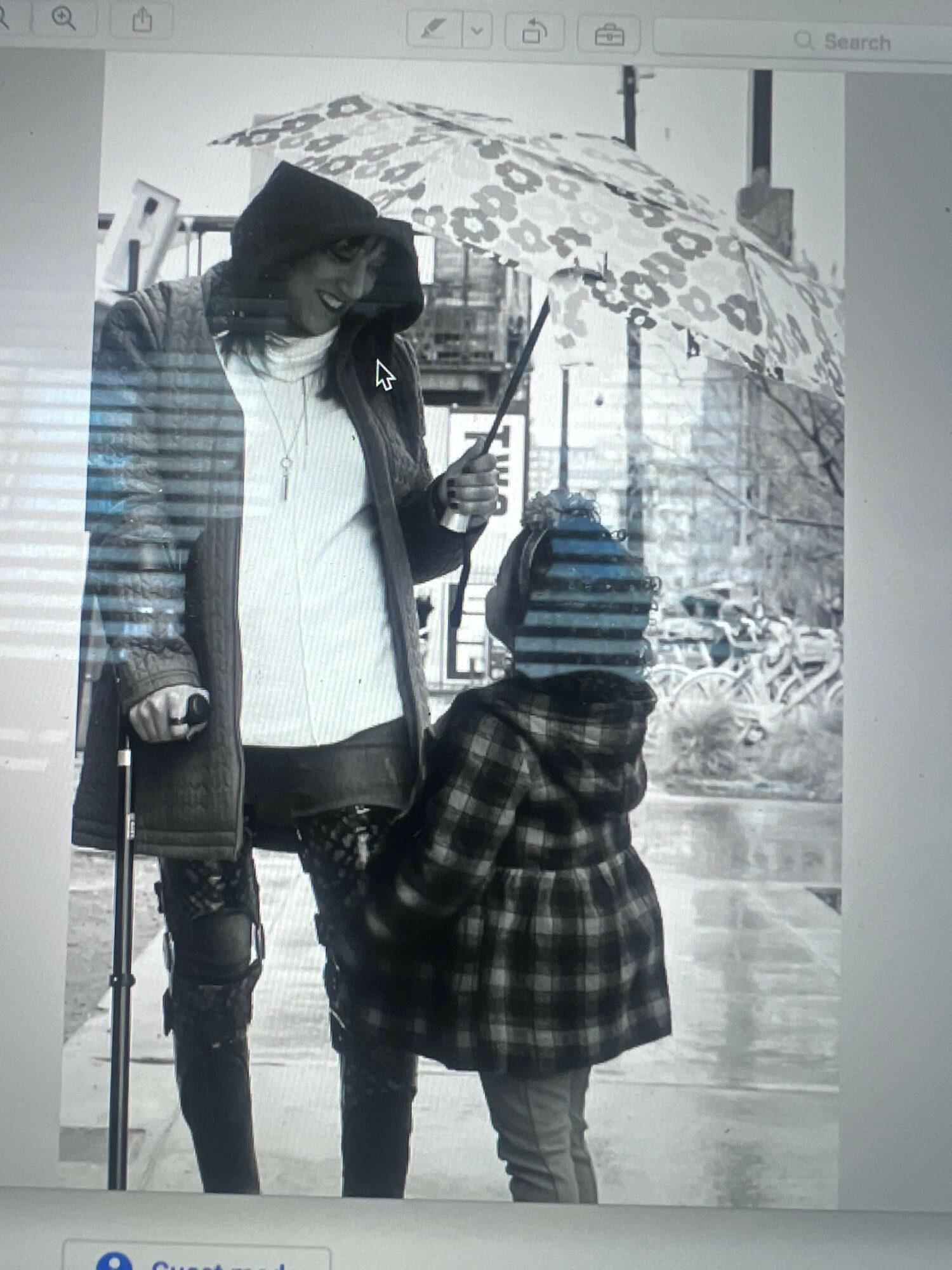 Woman and child with umbrella standing on wet street, buildings in background, black and white photo.